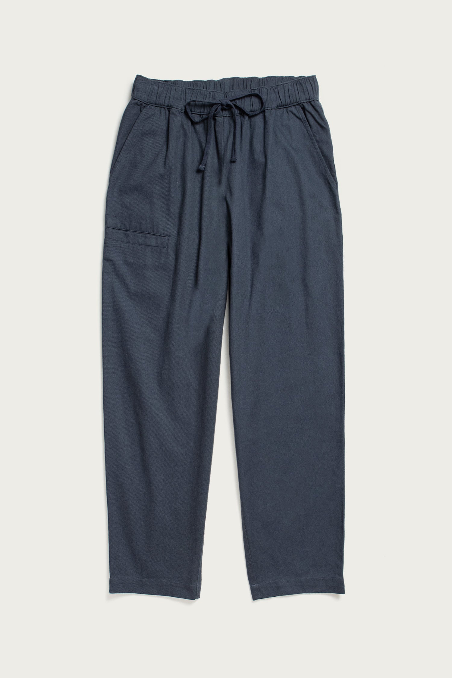 The Bridge & Burn Lark Pant in Dark Slate features a loose fit, elastic waist with drawstring, and a single patch pocket on the left side, shown laid flat against a plain light background.