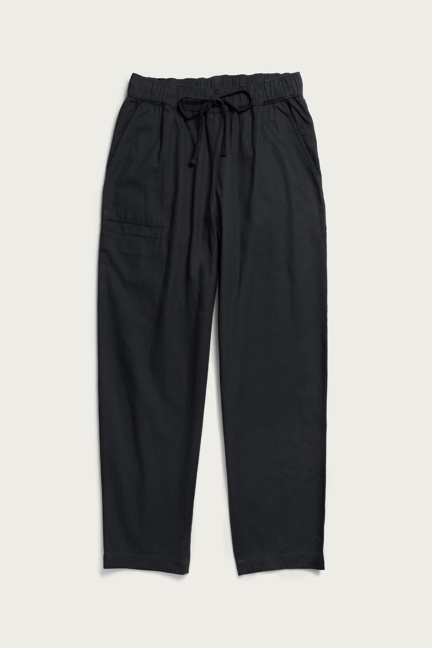The Bridge & Burn Lark Pant in Soft Black features a relaxed fit, organic cotton fabric, elastic waistband with drawstring, side pockets, and a right patch pocket. Pants are shown laid flat on a light background.