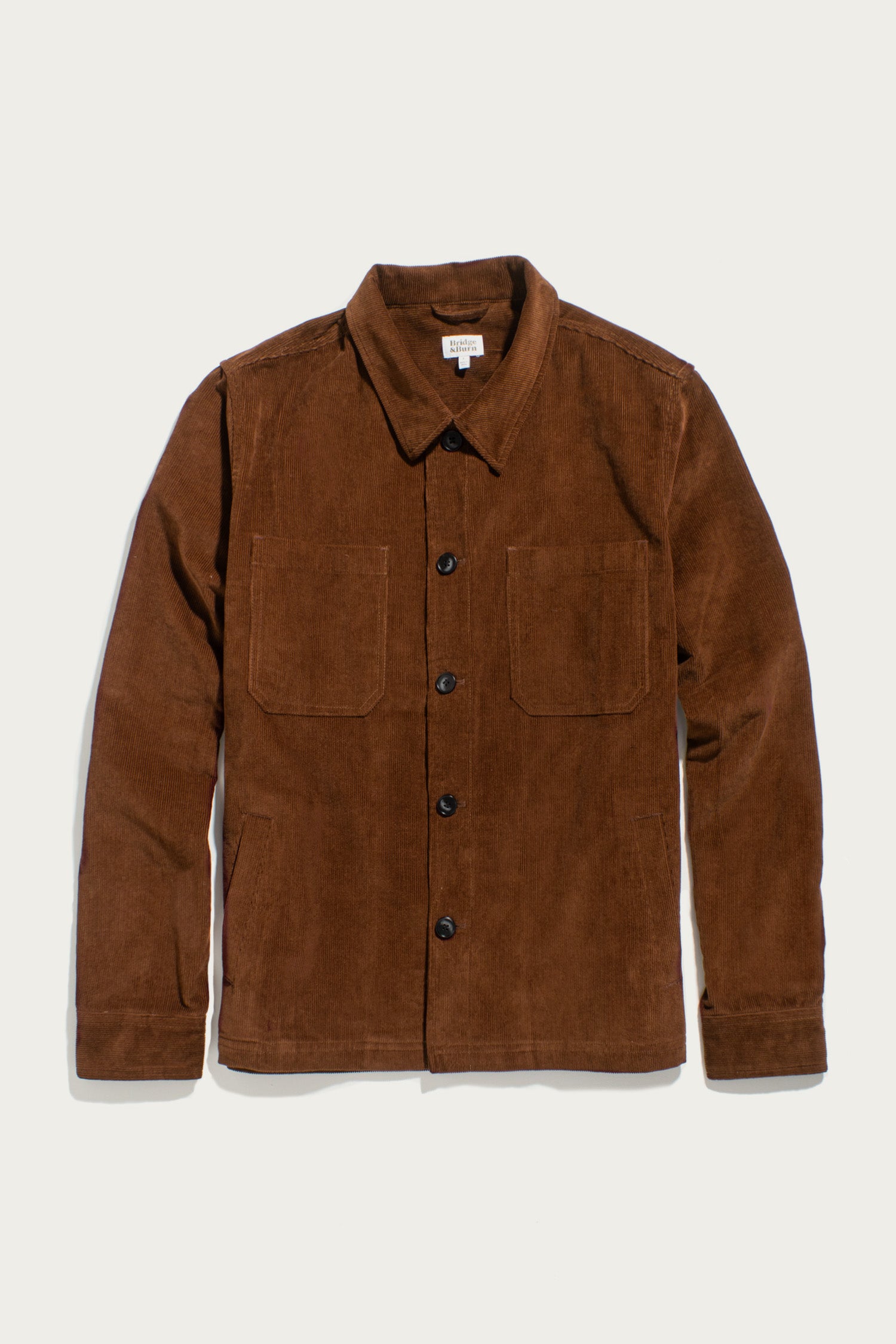 The Bridge & Burn Banks Shirt Jacket in Saddle Brown features a corduroy build, collared neckline, long sleeves, black front buttons, and two chest pockets—a timeless workwear essential.