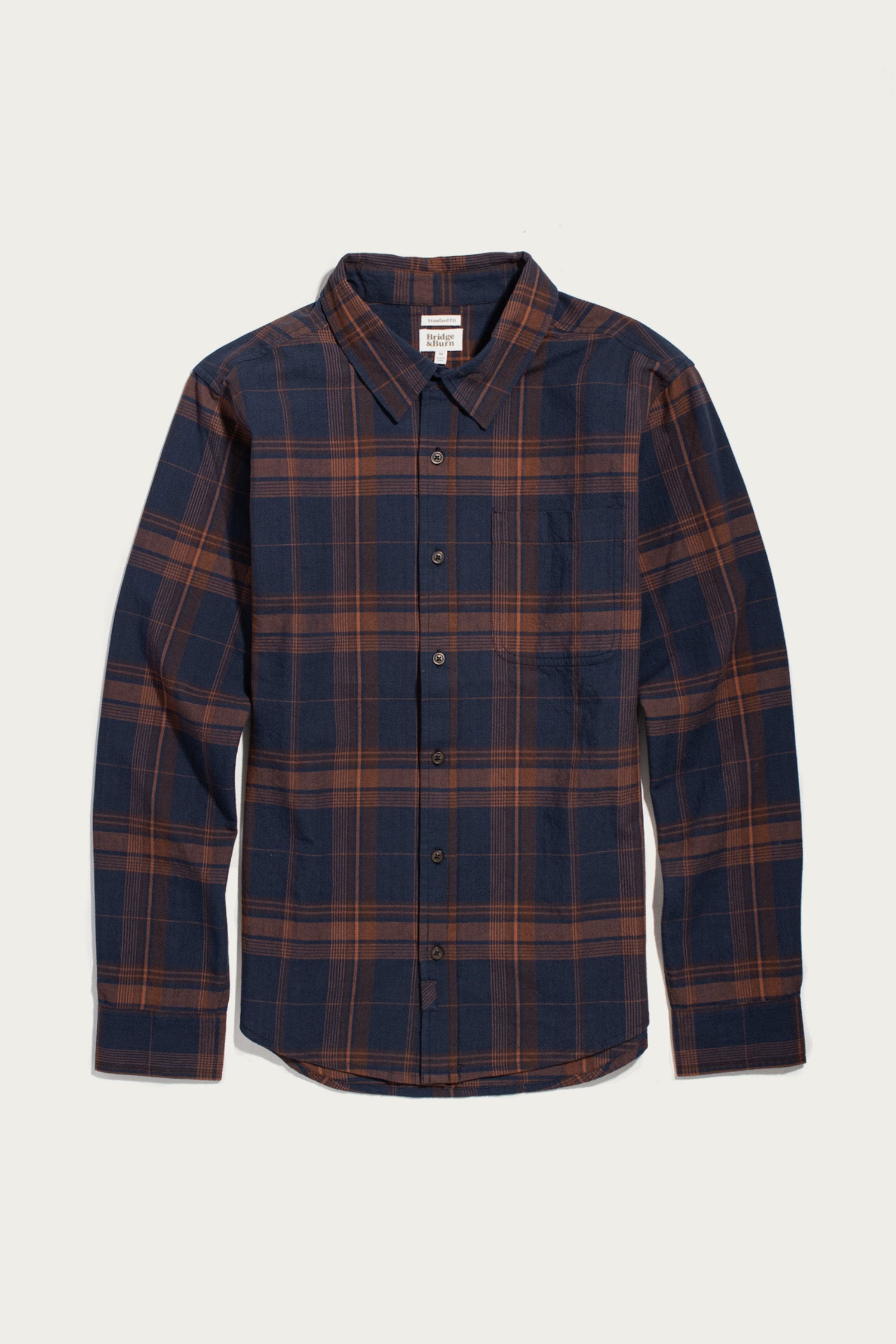 The Bridge & Burn Larson Shirt in Cinder Plaid is a classic-fit, long-sleeve button-up crafted from organic cotton with a navy blue and brown brushed flannel plaid pattern, featuring a classic collar and front pocket, shown laid flat on a white background.