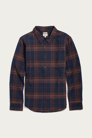 The Bridge & Burn Larson Shirt in Cinder Plaid is a classic-fit, long-sleeve button-up crafted from organic cotton with a navy blue and brown brushed flannel plaid pattern, featuring a classic collar and front pocket, shown laid flat on a white background.