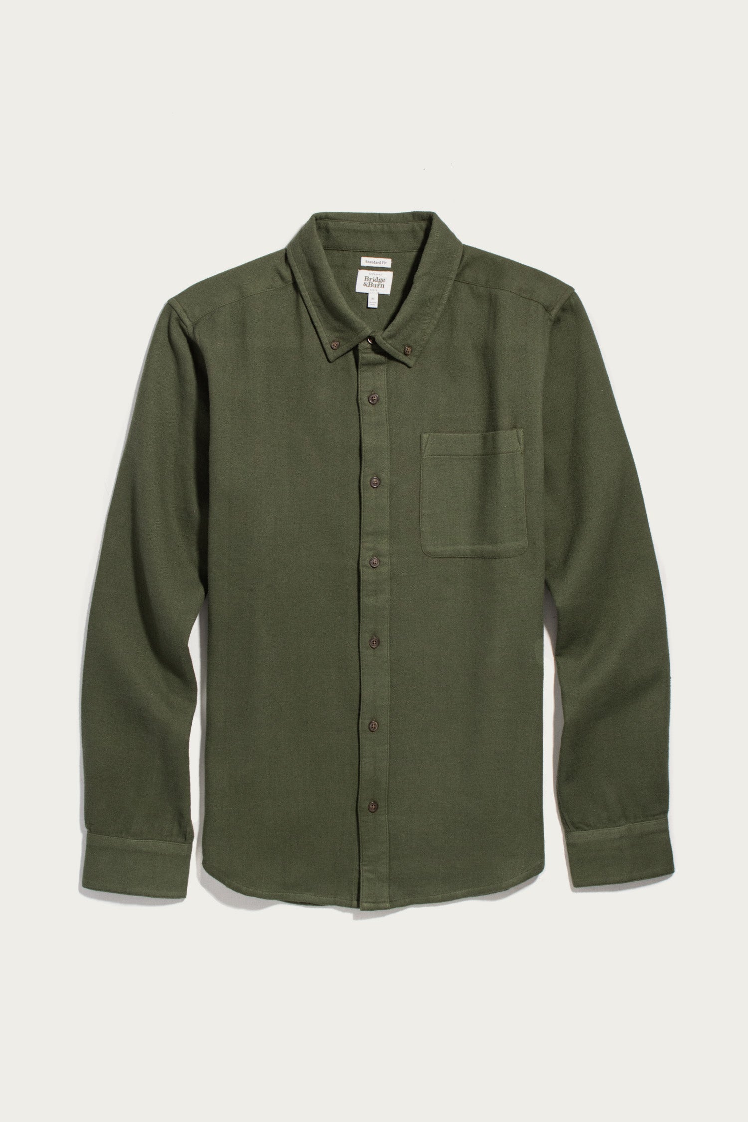 Bridge & Burn’s Sutton Slim Shirt in Pine Flannel features an olive green button-up design with long sleeves, a chest pocket, button-down collar, and brown buttons. Laid flat on a white background, this minimalist organic cotton shirt offers timeless style and comfort.