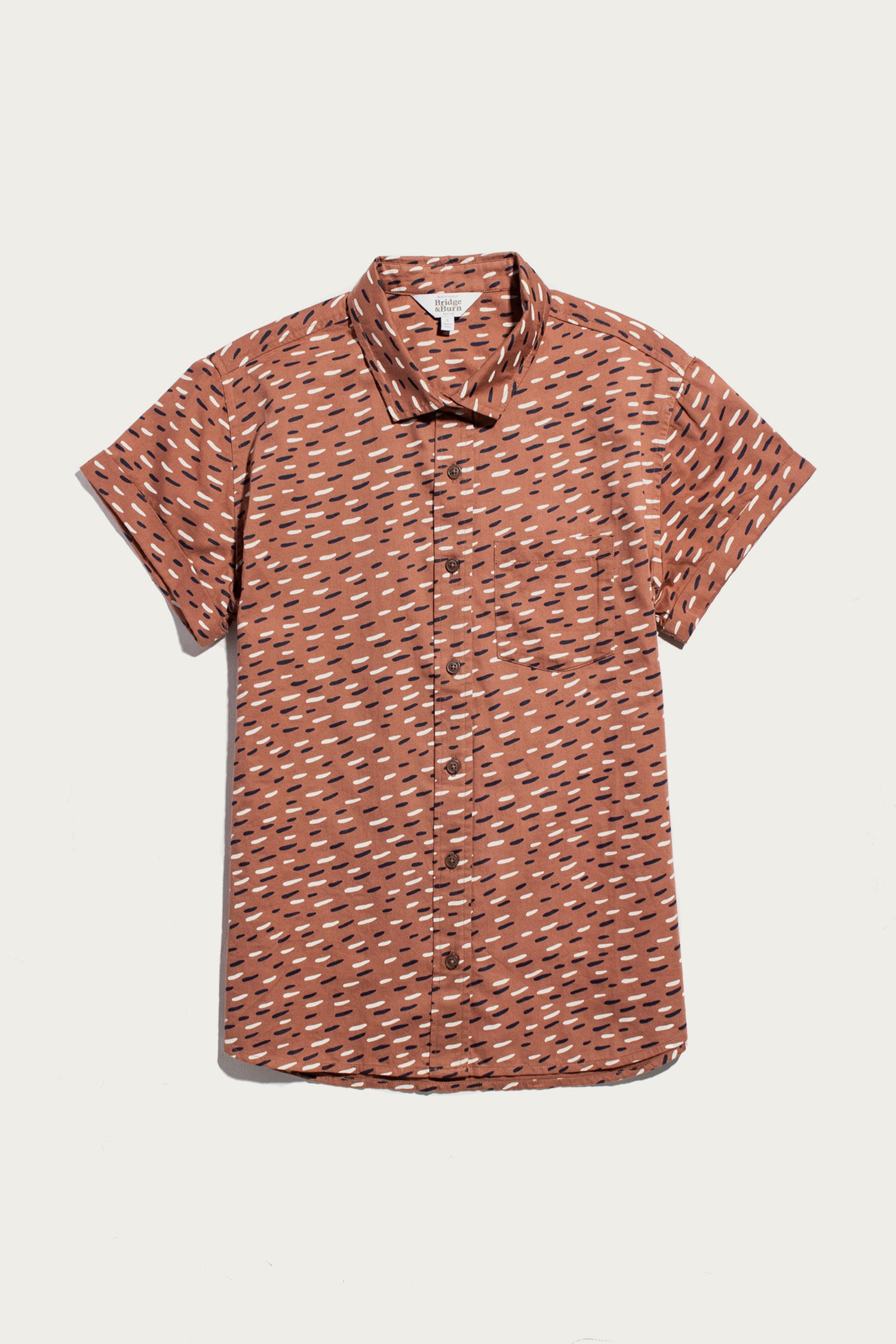 The Bea Shirt / Desert Rain by Bridge & Burn is a rust-colored, short-sleeve organic cotton button-down with scattered white and black lines, shown flat on a plain white background.