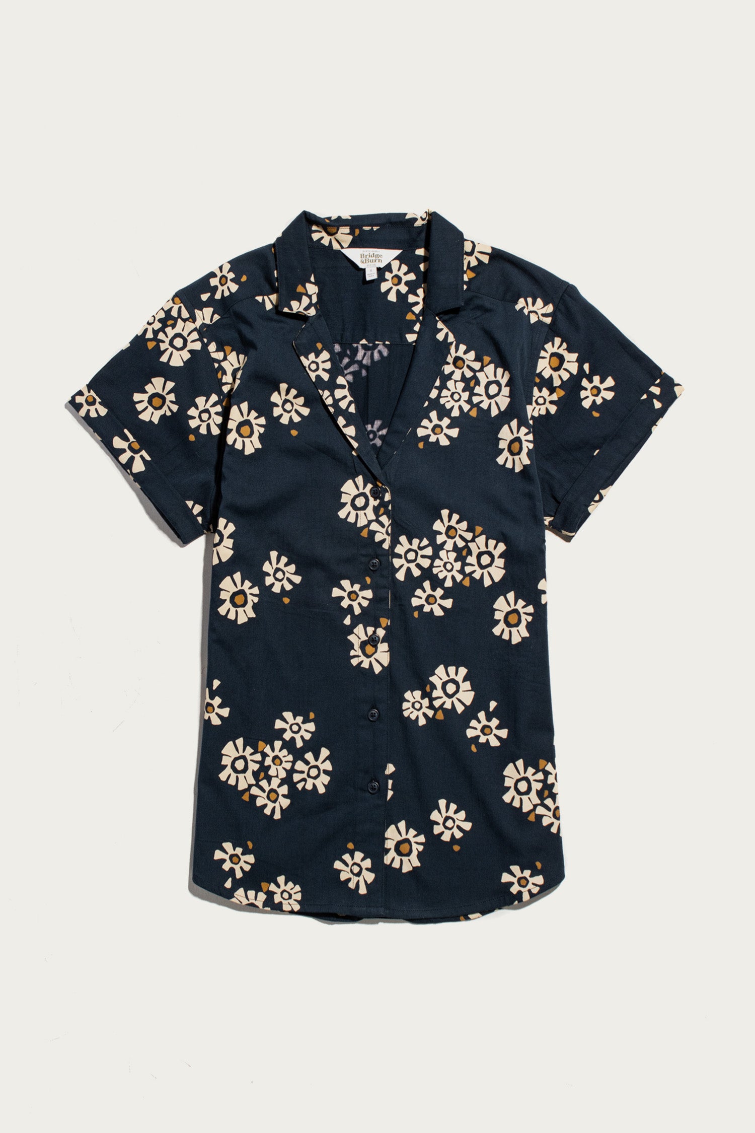 The Bridge & Burn Innes Shirt in Night Garden is a relaxed-fit, short sleeve, button-up shirt with a dark navy base and white-yellow floral pattern, crafted from organic cotton. Displayed flat on a white surface.