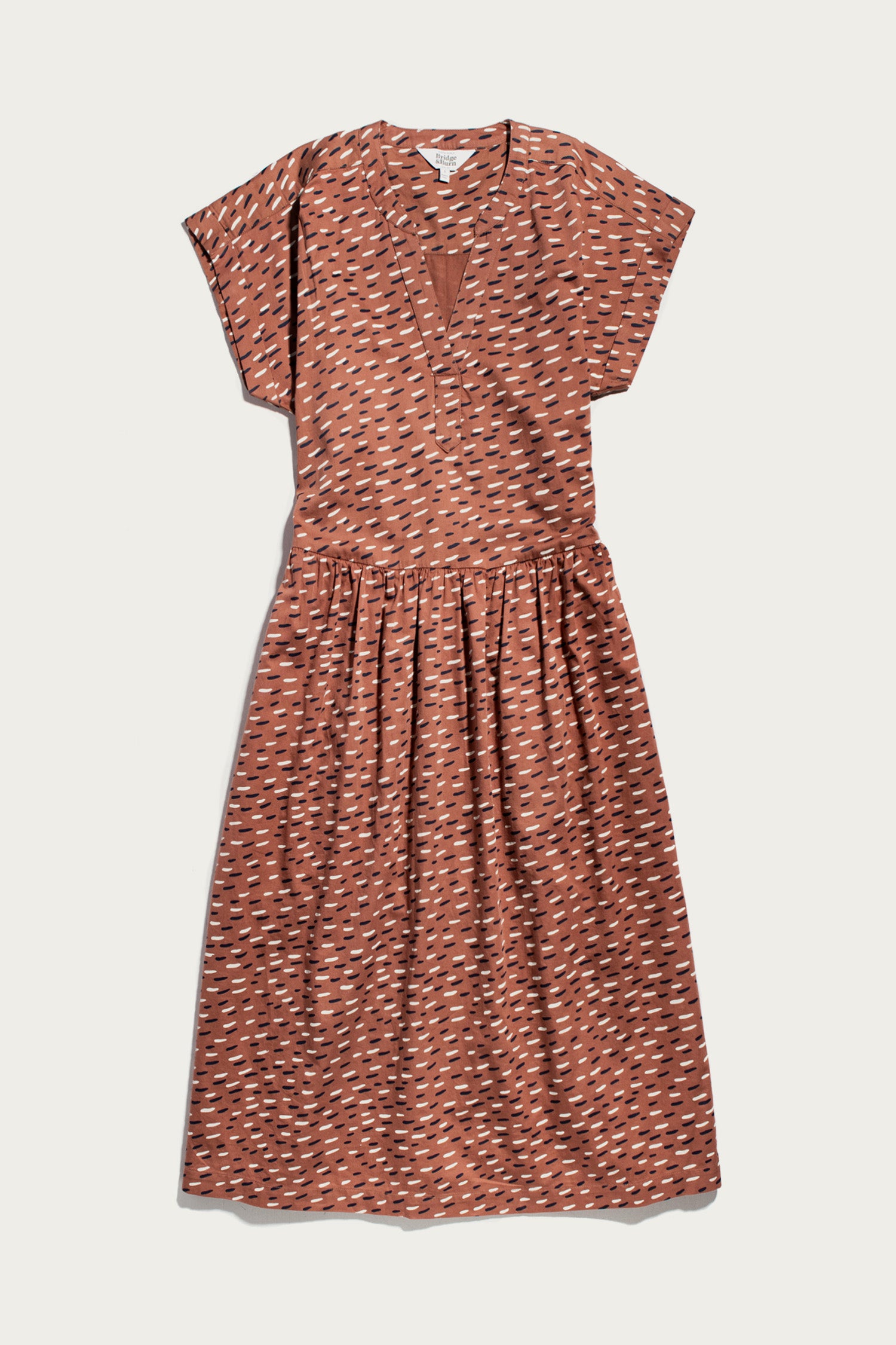 The Ira Dress / Desert Rain by Bridge & Burn is a rust midi pullover with short dolman sleeves, v-neckline, gathered waist, and an abstract white and black dash pattern.