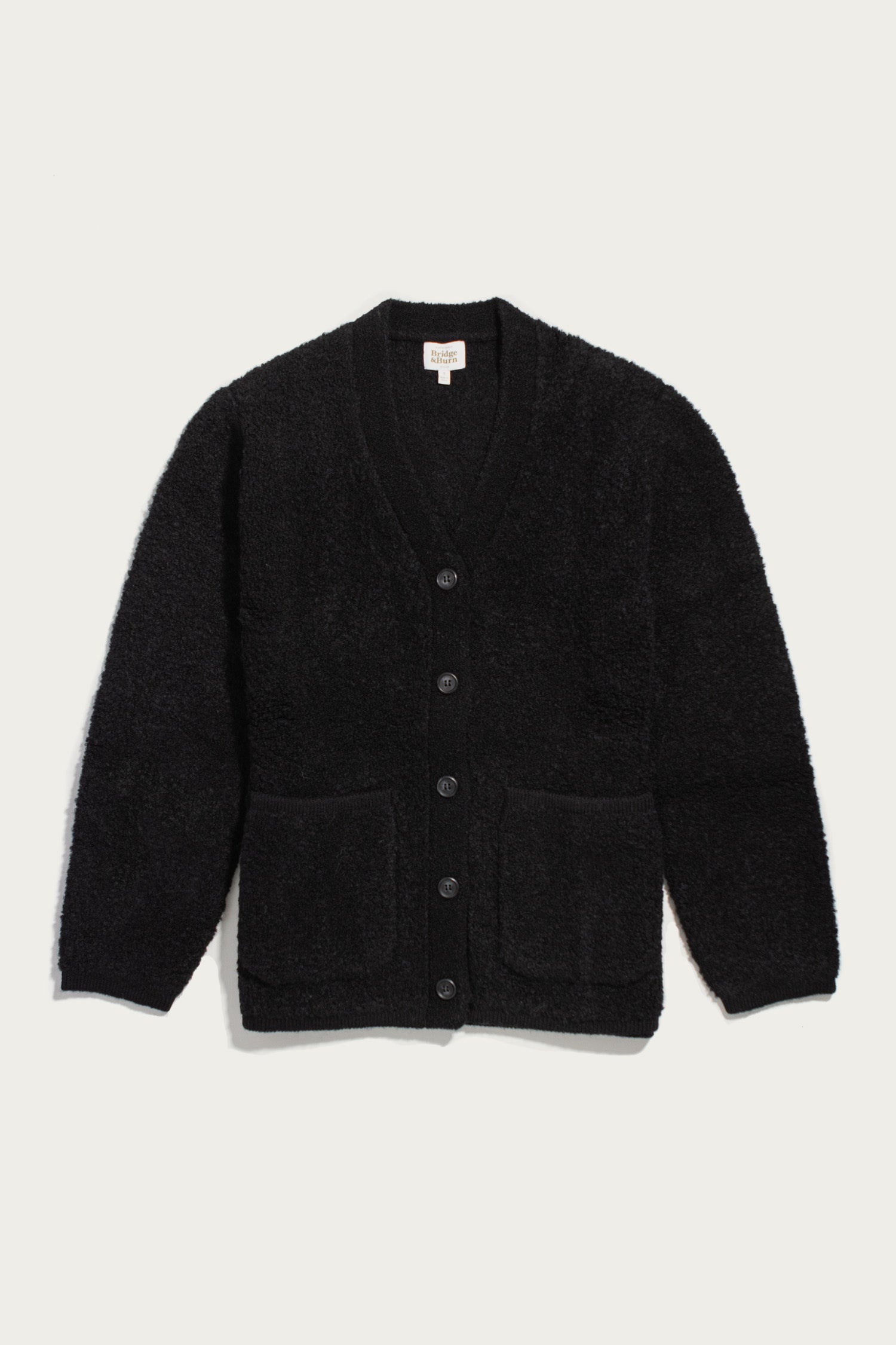 Whit Cardigan by Bridge & Burn in black, featuring a long-sleeve V-neck button-up design with two front pockets, shown flat on a white background. The textured knit fabric looks soft and inviting.