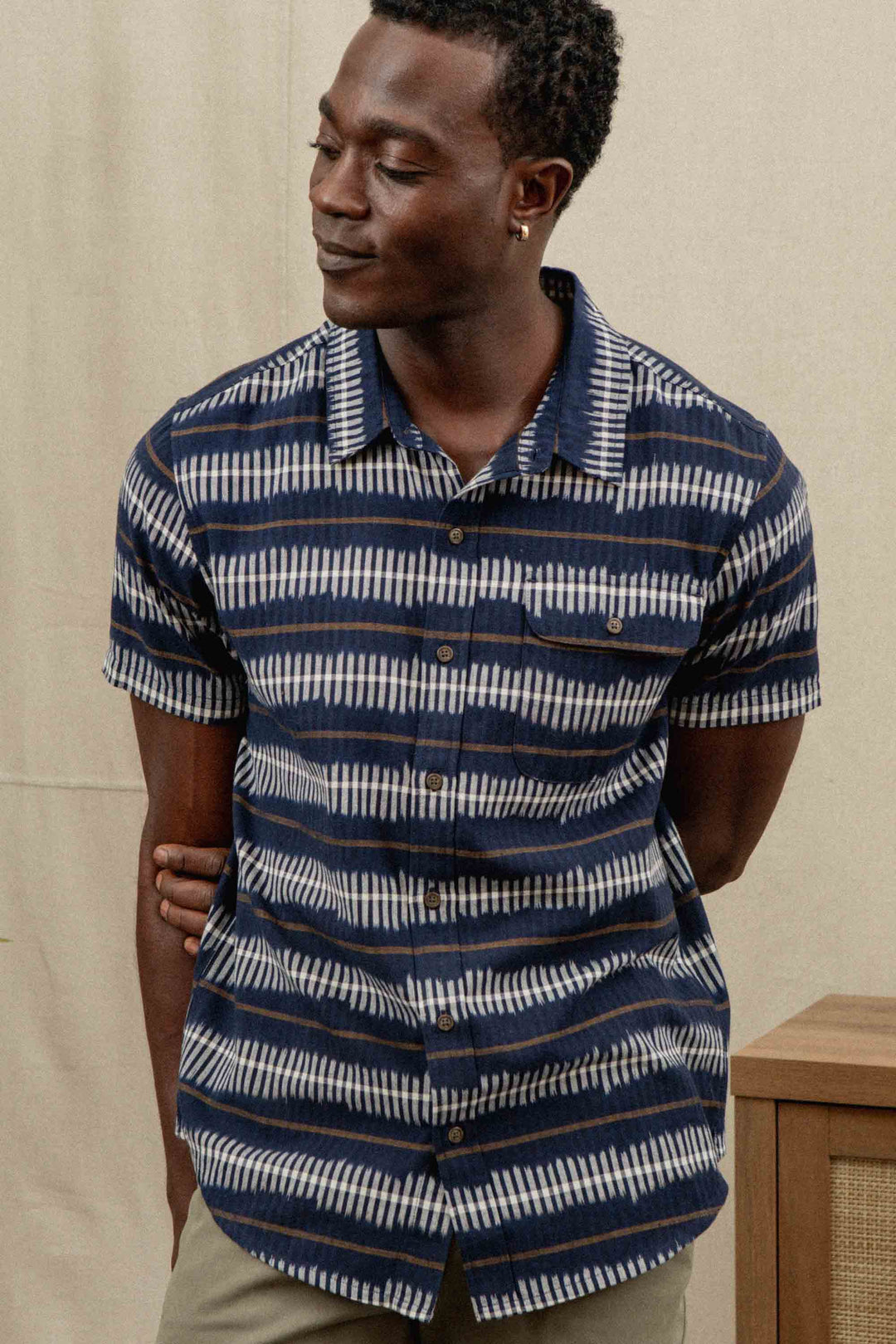 A man poses with a smile, arms behind his back, wearing the Bridge & Burn Marten Shirt in Dusk Mirage—featuring navy blue and white stripes—against a neutral background.