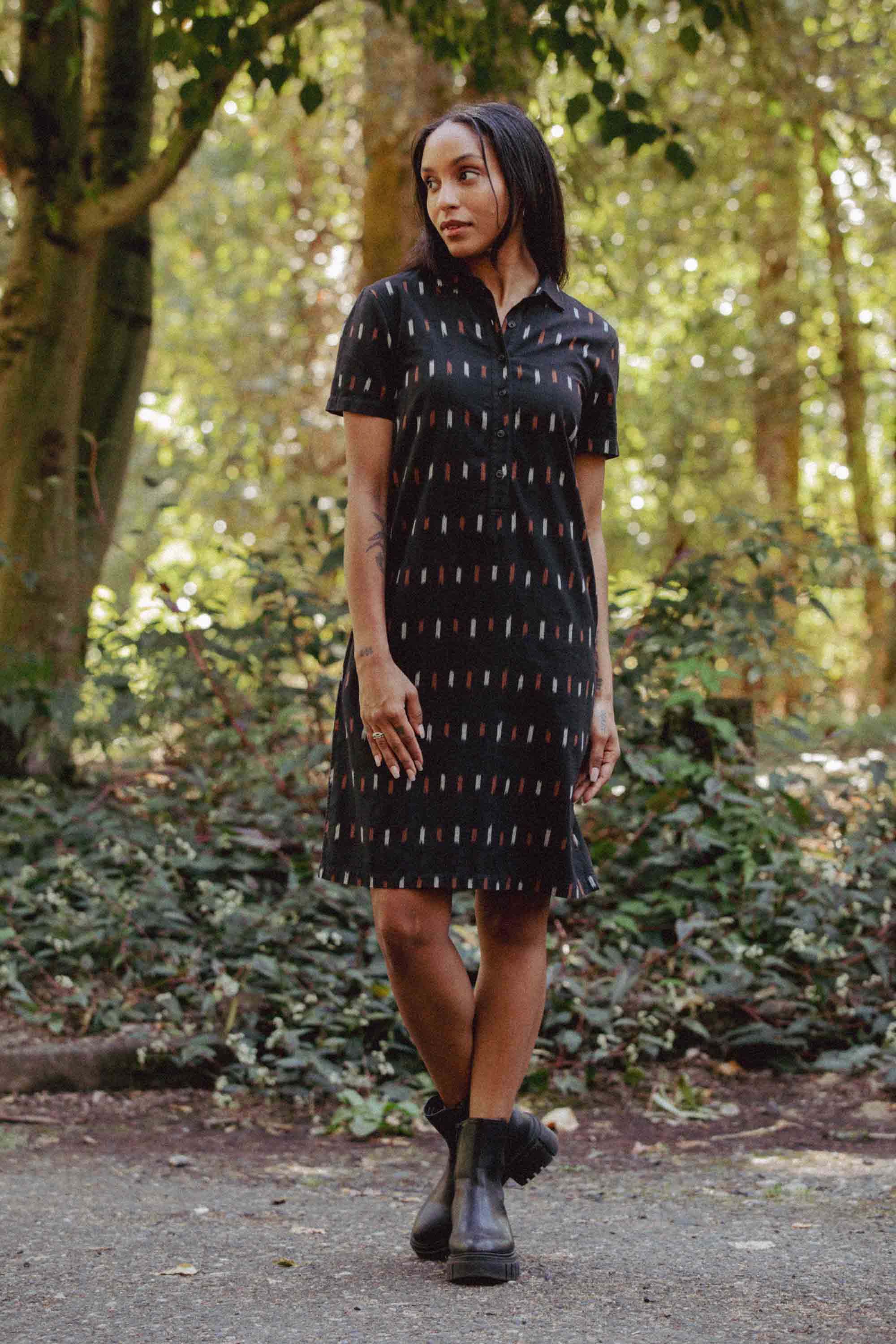 The Delia Dress by Bridge & Burn in Dotted Horizon is a short-sleeved, knee-length black organic cotton shirt dress with a collar, buttoned front, and vertical orange, white, and beige rectangle pattern.
