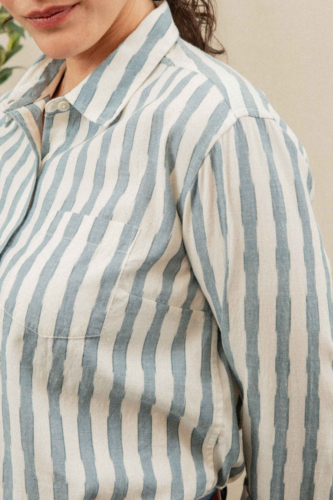 A close-up of a person wearing the Bridge & Burn Haley Shirt in Beach Stripe—a relaxed fit, button-up cotton overshirt with vertical blue and white stripes and a chest pocket. The person's face shows a slight smile.