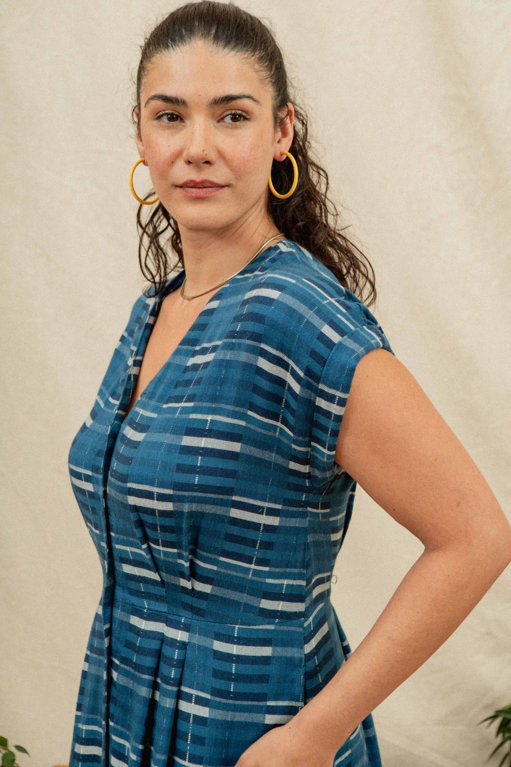 The Eileen Dress by Bridge & Burn in Stormcrest Stripe is a blue fit-and-flare with short sleeves, knee-length A-line skirt, white and navy plaid pattern, front buttons, V-neckline, and a slightly gathered waist.
