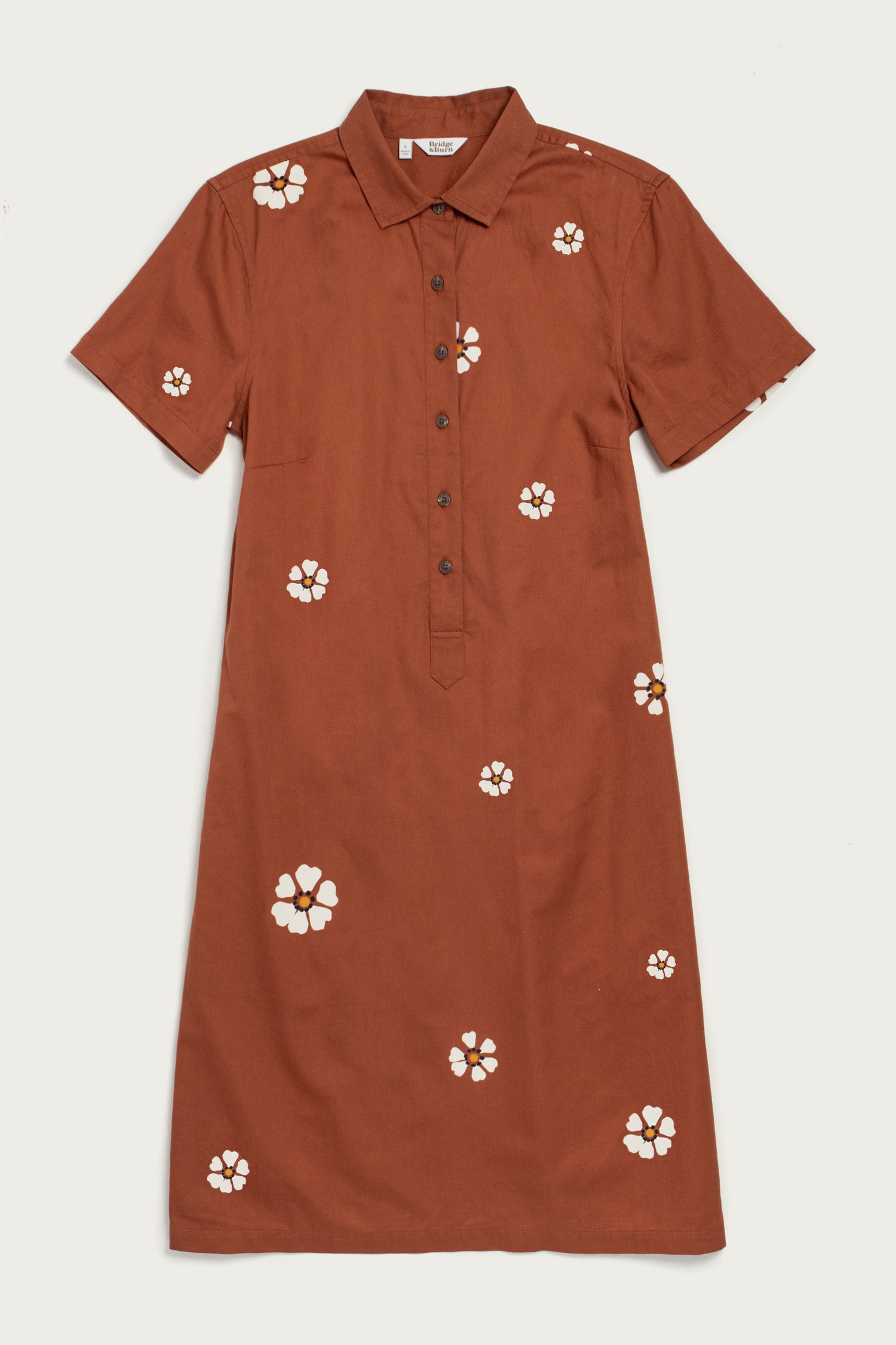 The Delia Dress in Redstone Bloom by Bridge & Burn is a short-sleeved, knee-length organic cotton shirt dress with front buttons and scattered white-and-yellow flower prints. It features a straight cut for a simple look.