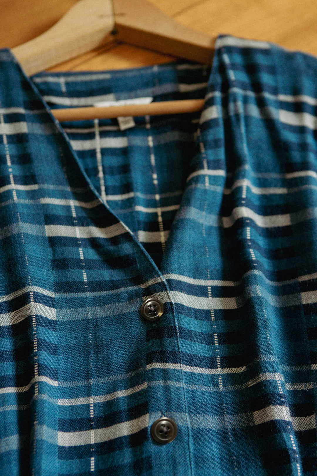 A close-up of the Bridge & Burn Eileen Dress in Stormcrest Stripe, featuring blue and white stripes and subtle dolman sleeves, hanging on a wooden hanger against a wooden background.