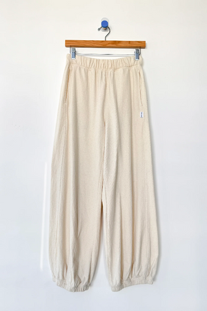 Le Bon Shoppe - Balloon Pant / Natural: Cream-colored, loose-fitting balloon leg pants made from undyed cotton with elastic waistband and cuffs by Le Bon Shoppe, shown hanging on a wooden hanger against a plain white wall.