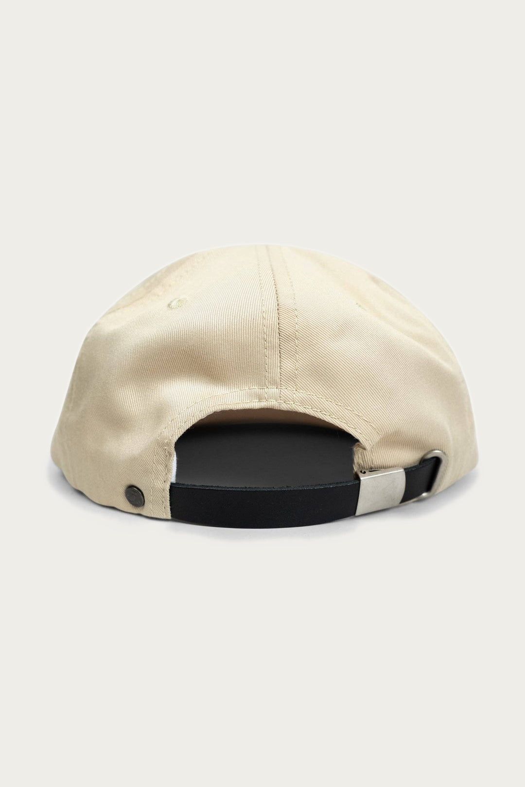 The Iron & Resin - Good Luck Hat in tan, made of cotton twill, is shown from the back with a black adjustable strap and metal buckle for size adjustment. The cap is set against a light, neutral background.