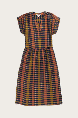 The Ira Dress by Bridge & Burn features knee-length, short dolman sleeves, a v-neck, Alpenglow Stripe pattern in mustard yellow, rust orange, navy blue, and black. Made from eco-friendly viscose with a gathered waist and relaxed fit.