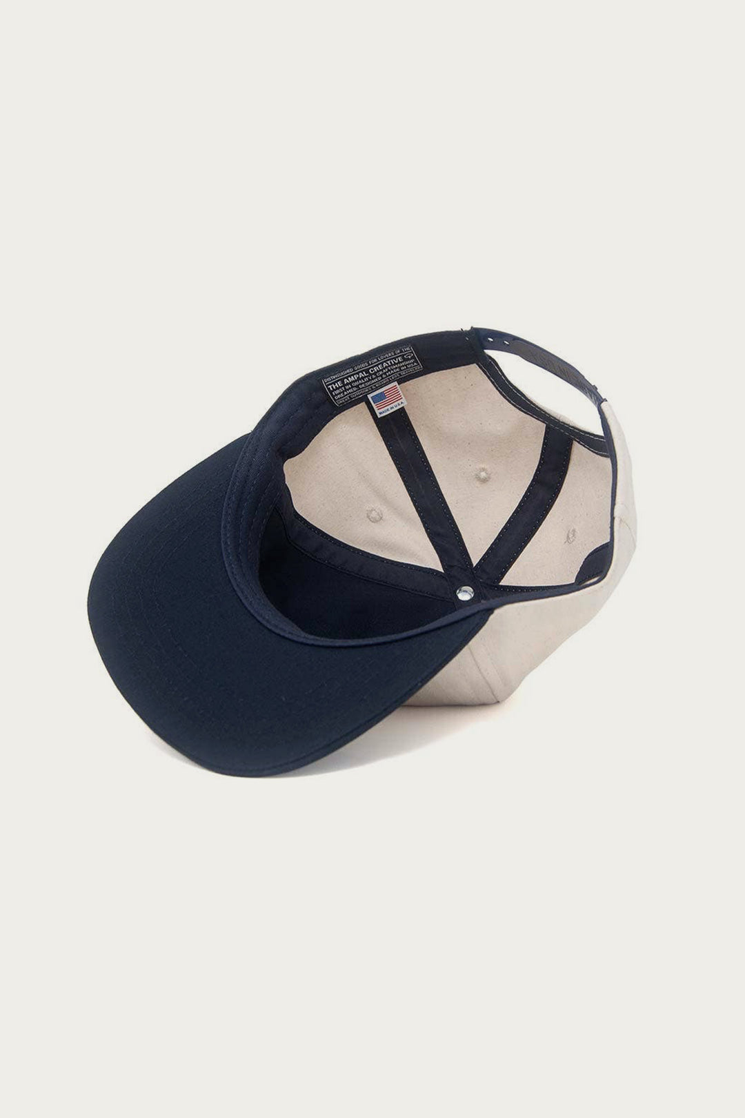 The Ampal Creative - Don't Think Twice Snapback in navy is shown upside down, displaying its inner lining, seam details, an American flag tag, and a distinctive Ampal patch inside.