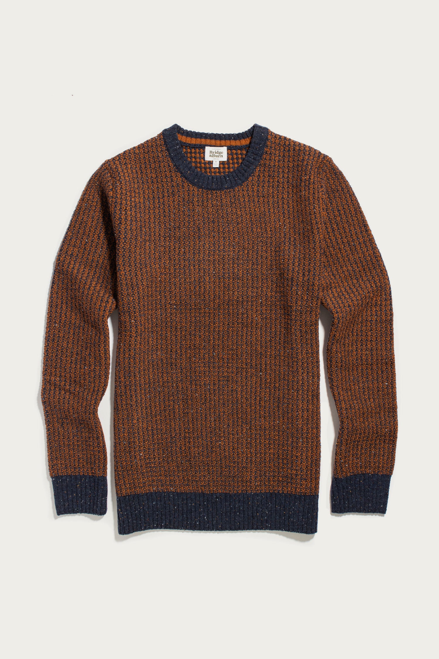 The Brighton Sweater in Autumn Tide by Bridge & Burn, a brown waffle knit sweater with a textured pattern, features navy blue ribbed cuffs, collar, and hem. It is shown laid flat on a white background.