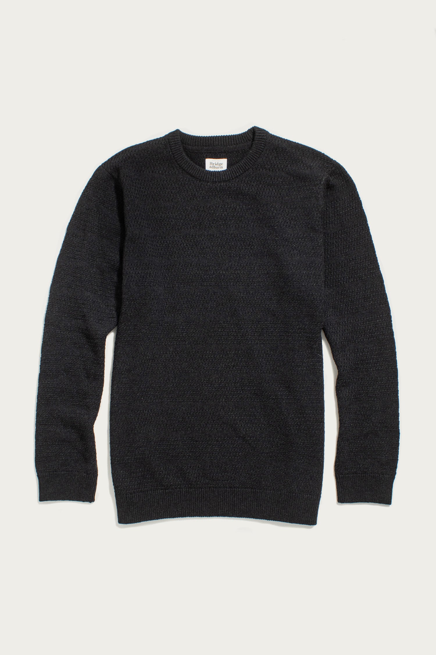 The Bridge & Burn Calder Sweater in Midnight, a black long-sleeve crew neck made from recycled materials, is laid flat on a white background. It features a textured knit pattern with ribbed cuffs, collar, and hem.
