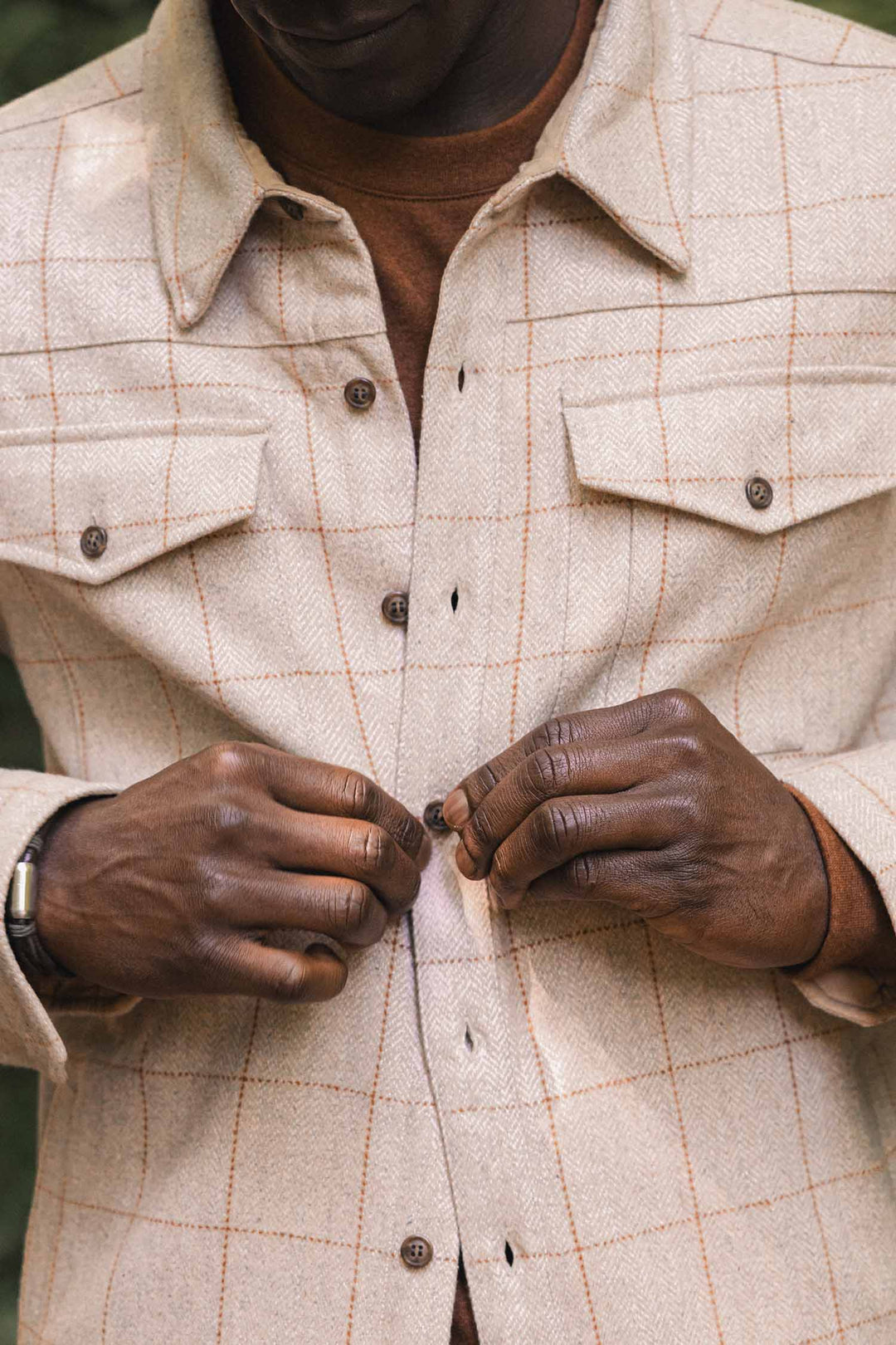 A person is fastening a button on the Bridge & Burn Fielding Shirt Jacket in Stonecross over a brown top. The focus is on their hands and torso; their face is not visible.