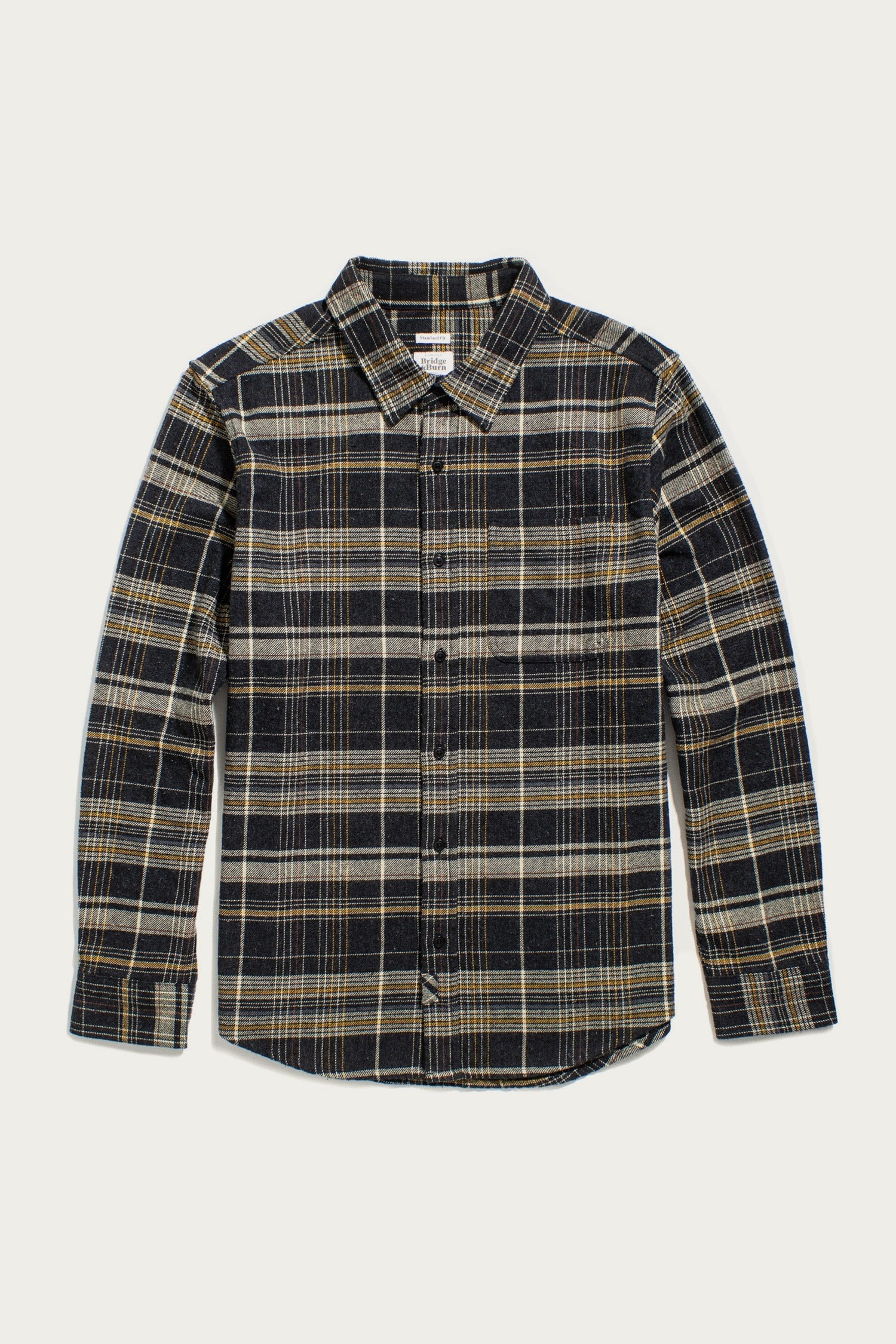 The Bridge & Burn Larson Shirt in Volcanic Plaid is a long-sleeve, button-up flannel with black, gray, and beige tones, a single chest pocket, and pointed collar. Made from recycled cotton. Laid flat on a white background.