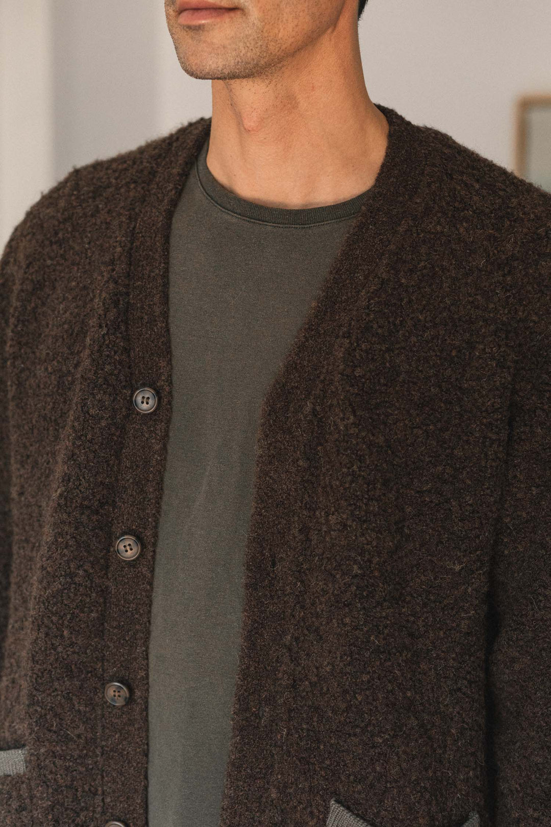 A person wearing the Bridge & Burn Mateo Cardigan in dark olive, featuring textured knit fabric and patch pockets, layered over a plain dark green shirt; the photo shows them from shoulders to chest with their face partially out of frame.