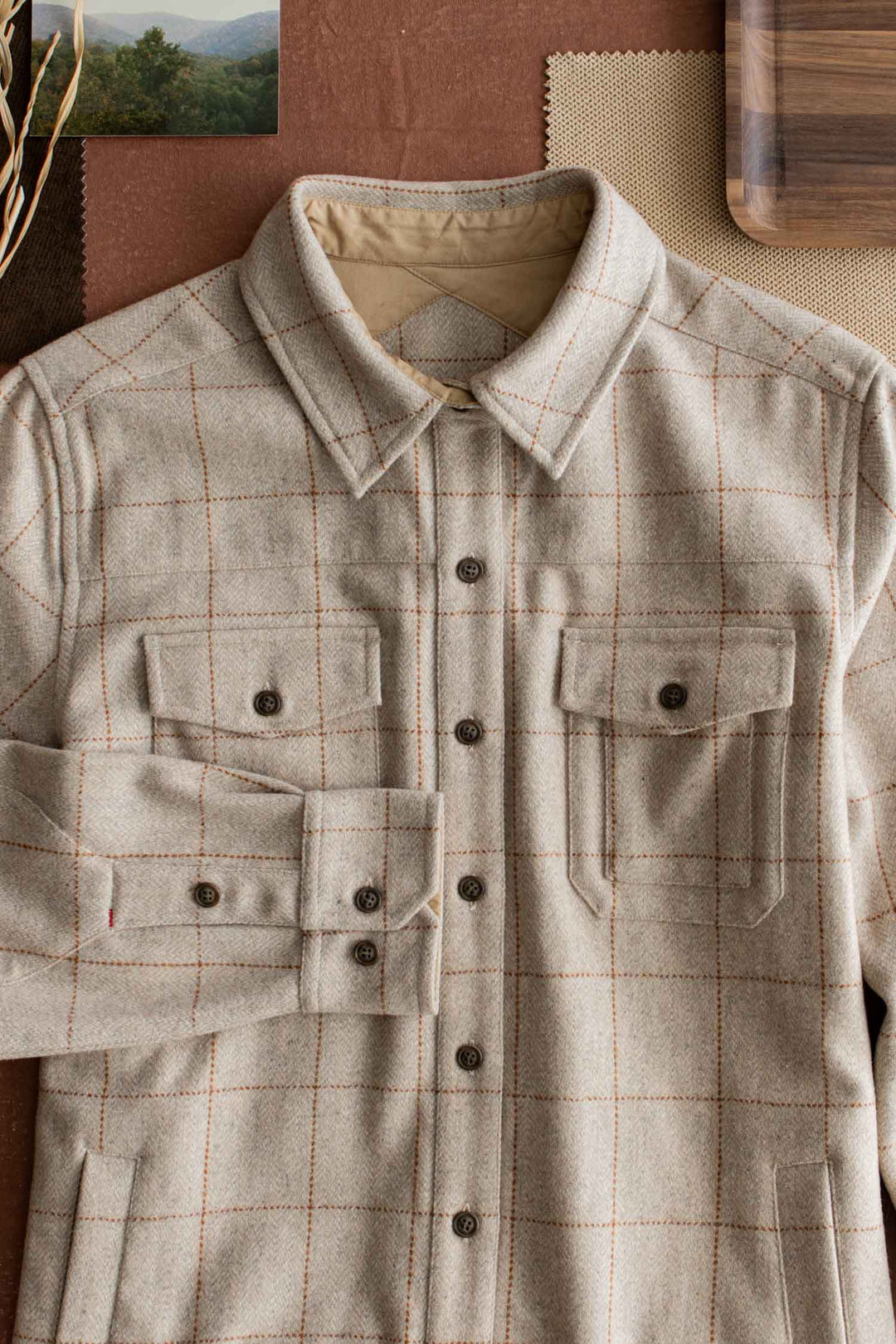 The Bridge & Burn Harlow Shirt Jacket in Stonecross is neatly laid out on a surface, surrounded by neutral fabric swatches, a wooden tray, and a small landscape photo in the top left corner.