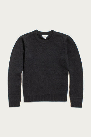 The Ansel Sweater in Midnight by Bridge & Burn is a dark gray crewneck with long sleeves, ribbed cuffs, hem, and collar, made from recycled fibers—a sustainable wardrobe essential.