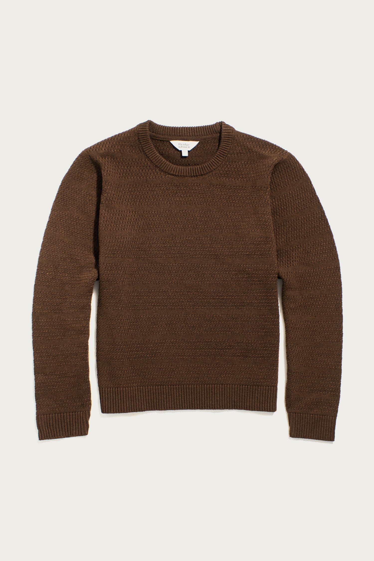 The Bridge & Burn Ansel Sweater in Walnut—a brown, mid-weight crewneck with ribbed cuffs, hem, and collar—made from recycled fibers is shown laid flat on a light background.