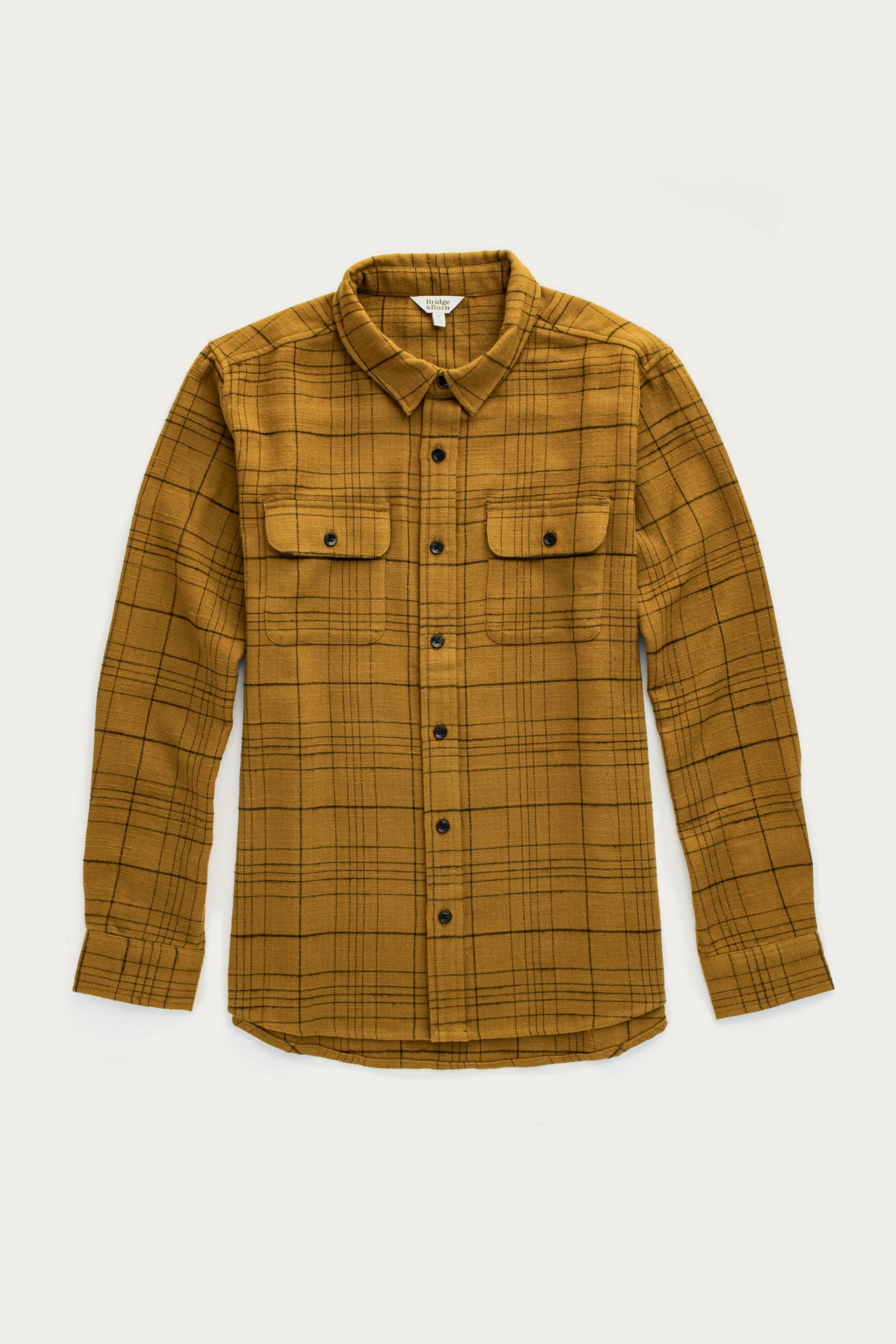 The Bridge & Burn Lenon Shirt in Golden Horizon Plaid is a mustard yellow, long-sleeve over-shirt with a black plaid pattern, front chest flap pockets, and a pointed collar, shown laid flat on a white background.