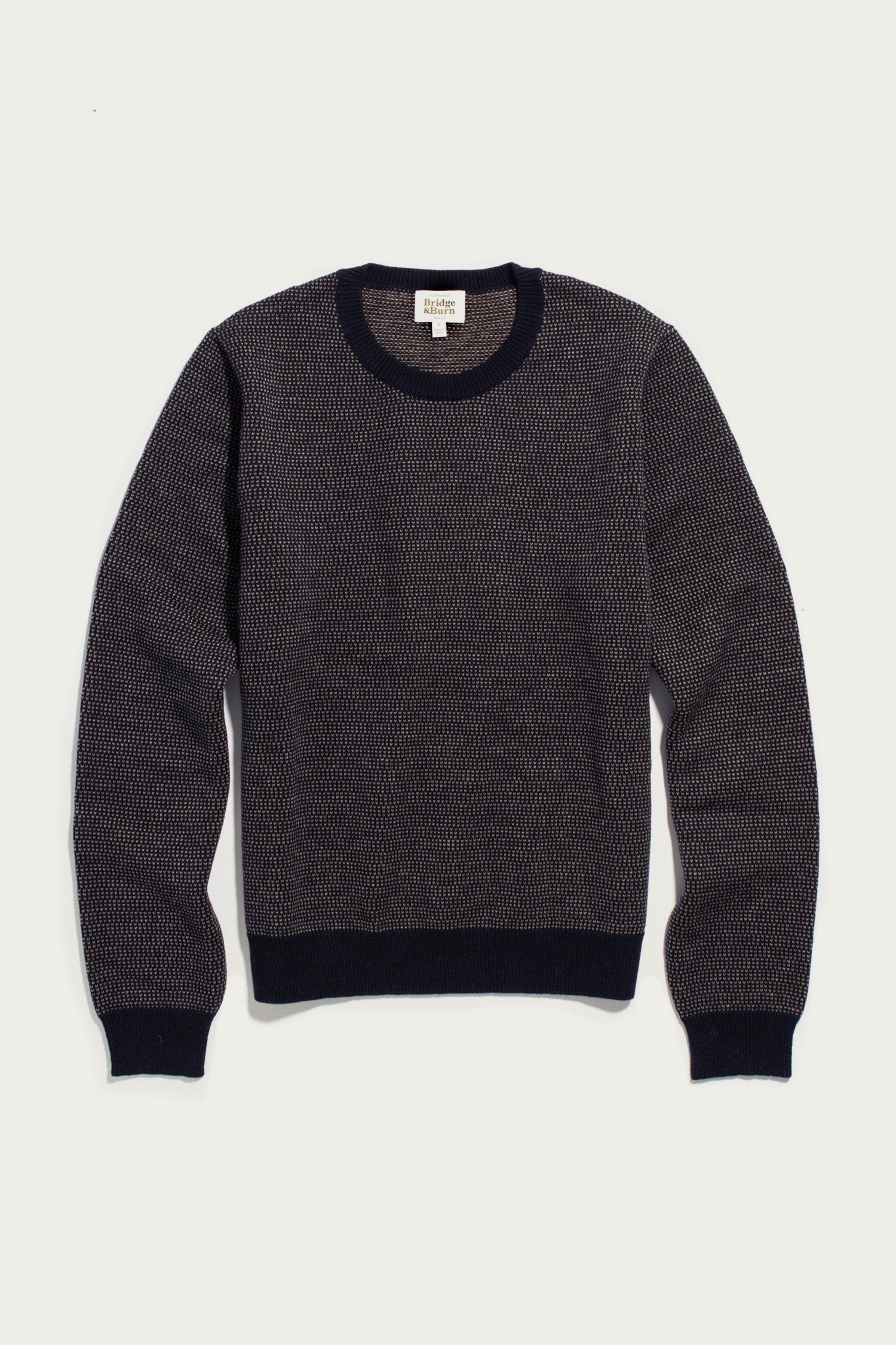 The Bridge & Burn Pickering Sweater in Harbor Mist features a long-sleeve crewneck design with a textured black and gray knit pattern, crafted from soft Merino wool. Solid black accents finish the cuffs, collar, and waistband. Made in accordance with the Responsible Wool Standard, the sweater is shown laid flat on a white background.