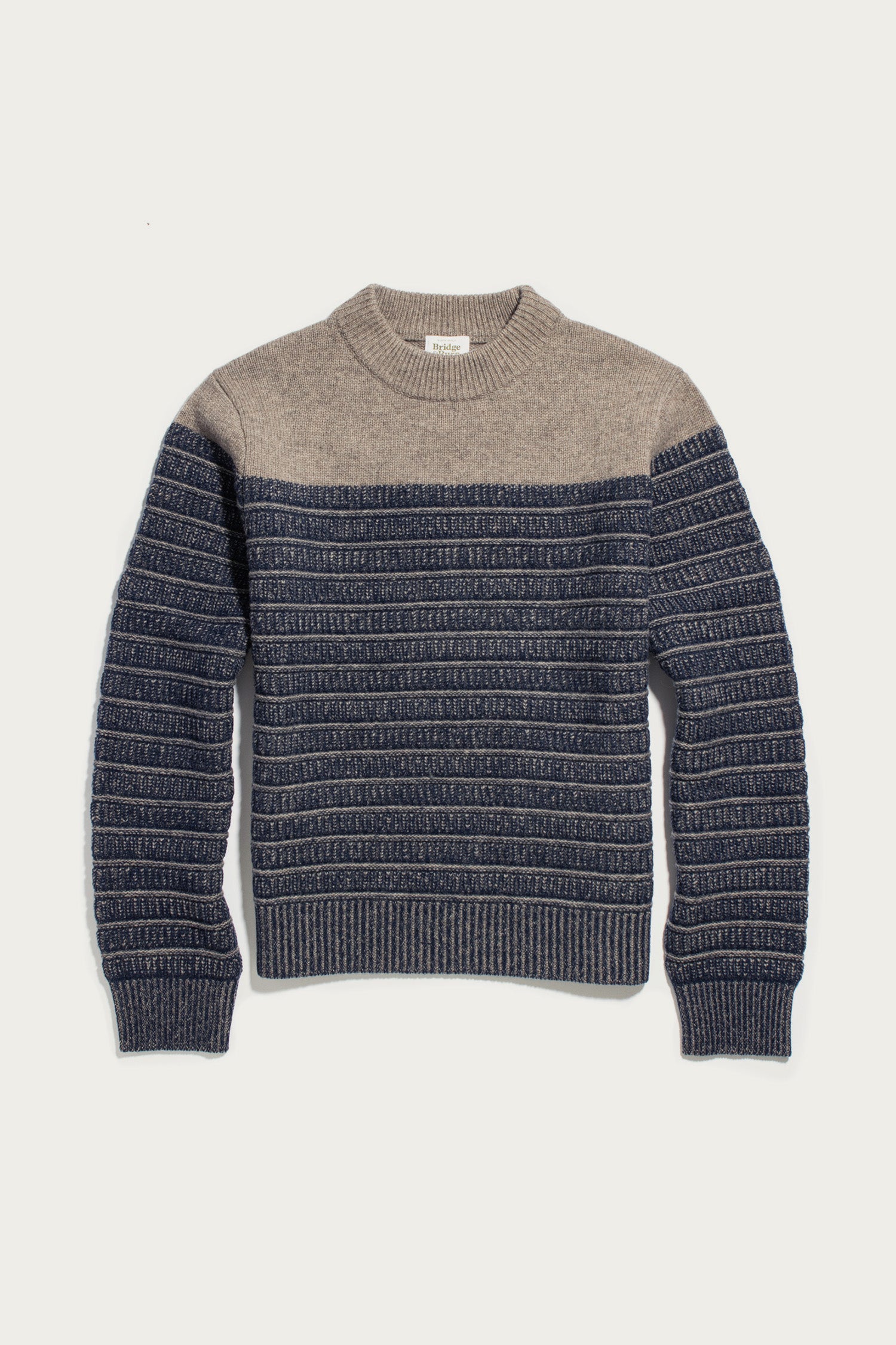 The Bridge & Burn Sabine Sweater in Mariner Stripe is a heavyweight merino wool sweater with a beige top and dark blue bottom, accented by horizontal textured stripes and finished with ribbed cuffs, hem, and a mock neck collar; shown laid flat on a white background.