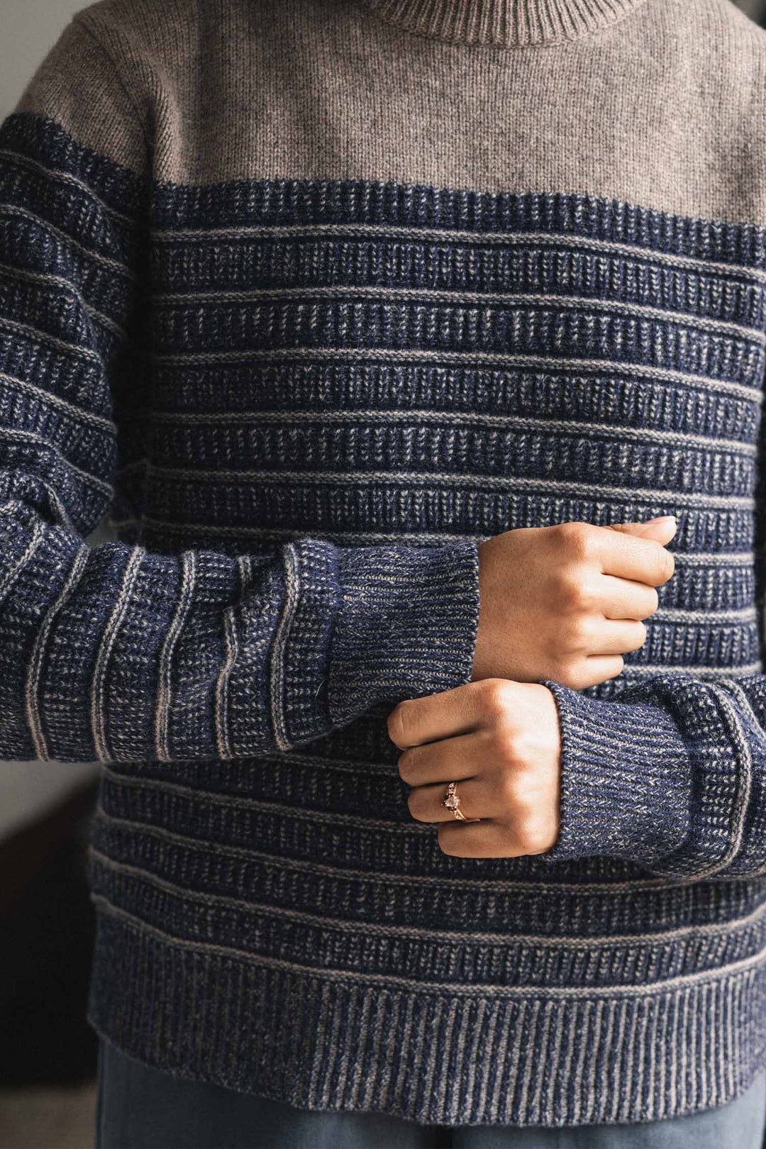 A person wearing the Bridge & Burn Sabine Sweater in Mariner Stripe adjusts their sleeve. Only their torso and hands are visible, with a ring on their left hand.