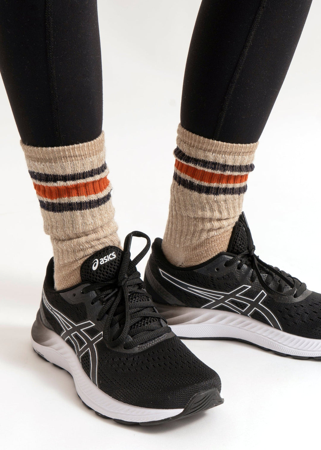 Someone wearing American Trench Merino Activity Crew socks in tan stands on a white background, paired with black leggings and black ASICS running shoes.