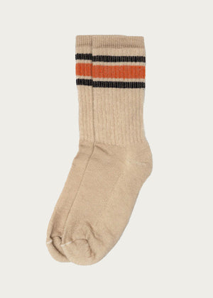A single American Trench - Merino Activity Crew sock in tan, featuring two black stripes and one orange stripe near the top, is displayed on a plain white background.