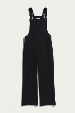 The Edie Overall in Black by Bridge & Burn is displayed flat on a white background, showcasing its wide-leg corduroy construction and relaxed fit, with adjustable shoulder straps, metal fasteners, and front pockets.