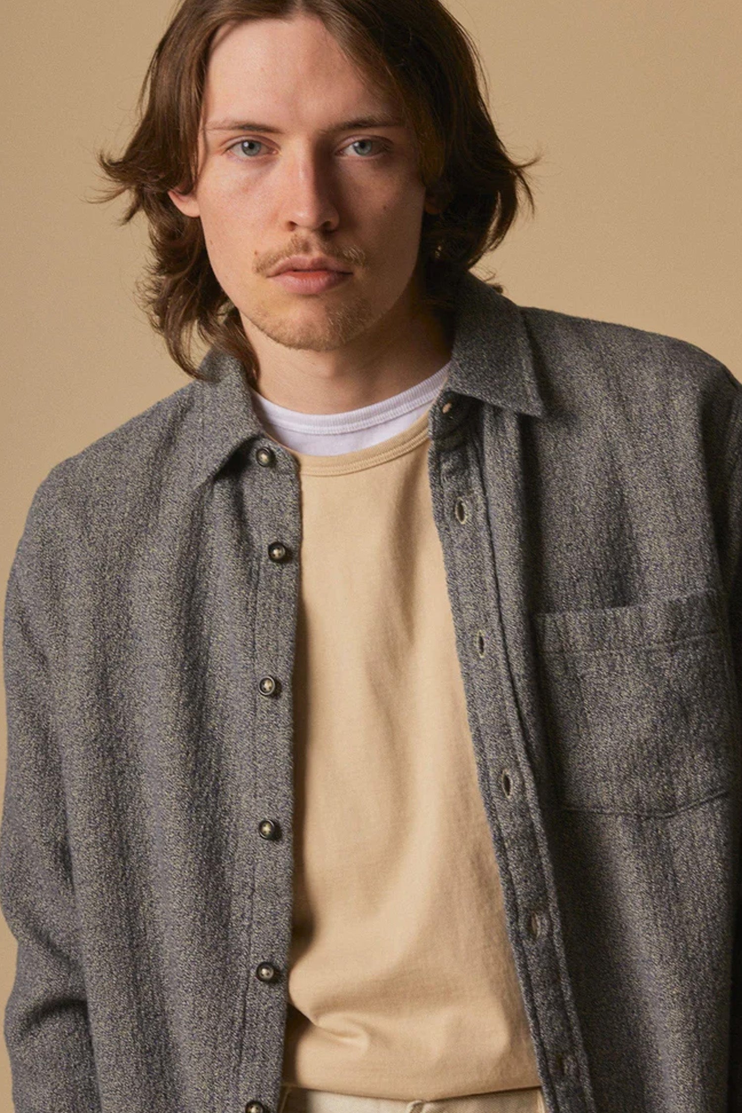 A man with shoulder-length brown hair and light facial hair wears the Corridor Pearl Boucle Shirt in navy, standing against a plain beige background and looking directly at the camera.