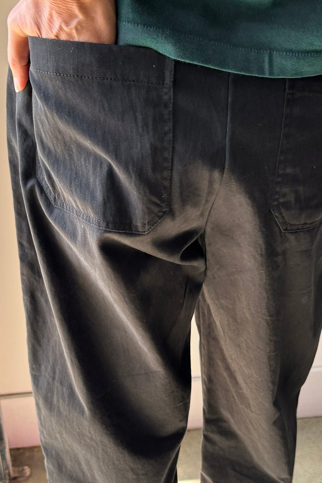 A person wearing the Le Bon Shoppe Gardener's Pant in Black, featuring a relaxed silhouette and visible back pockets, stands with one hand in a pocket. The top of the image reveals part of their shirt.