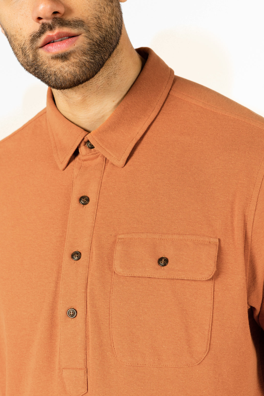A close-up of a man wearing the Bridge & Burn Gary Knit Pullover in Clay Red Jersey, shown from chin to mid-torso against a plain light background.