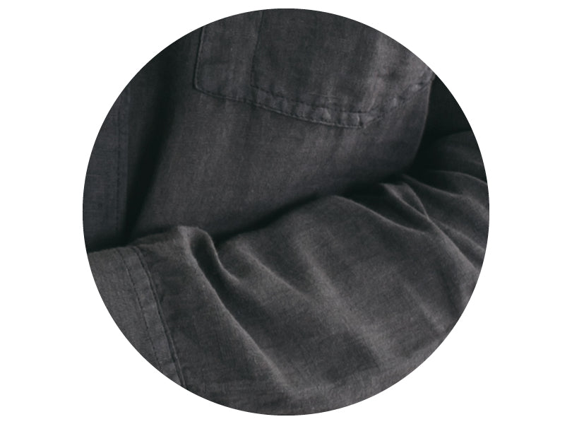Close-up of a dark gray shirt made of a soft, textured fabric, shown with a visible chest pocket and sleeve, photographed inside a circular frame.