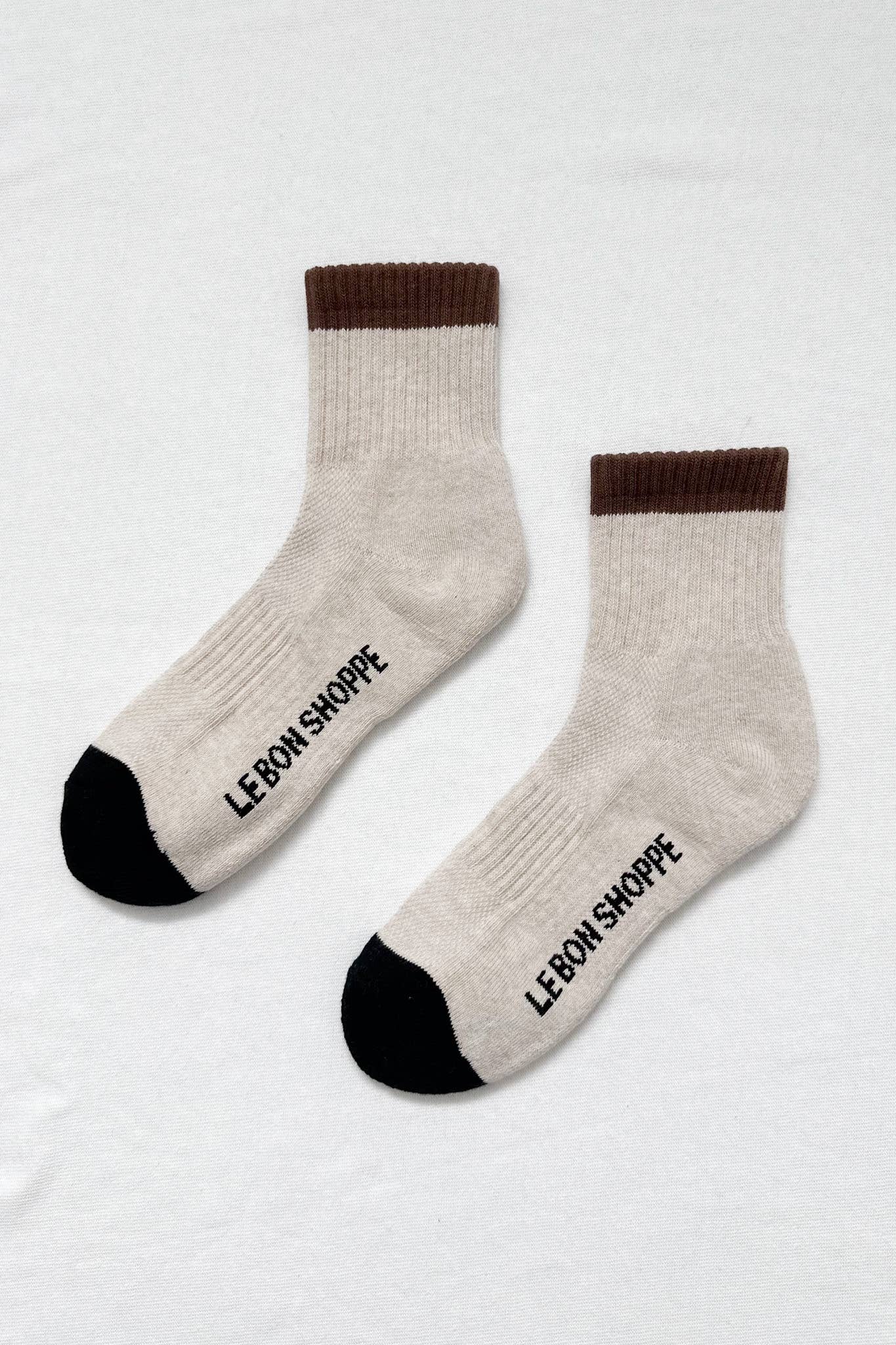 The Le Bon Shoppe Color Block Girlfriend Socks in Black Coffee feature cream, brown cuffs, and black toes—stylish socks with sporty flair and “LE BON SHOPPE” printed on the soles. Perfect for elevating any casual look.