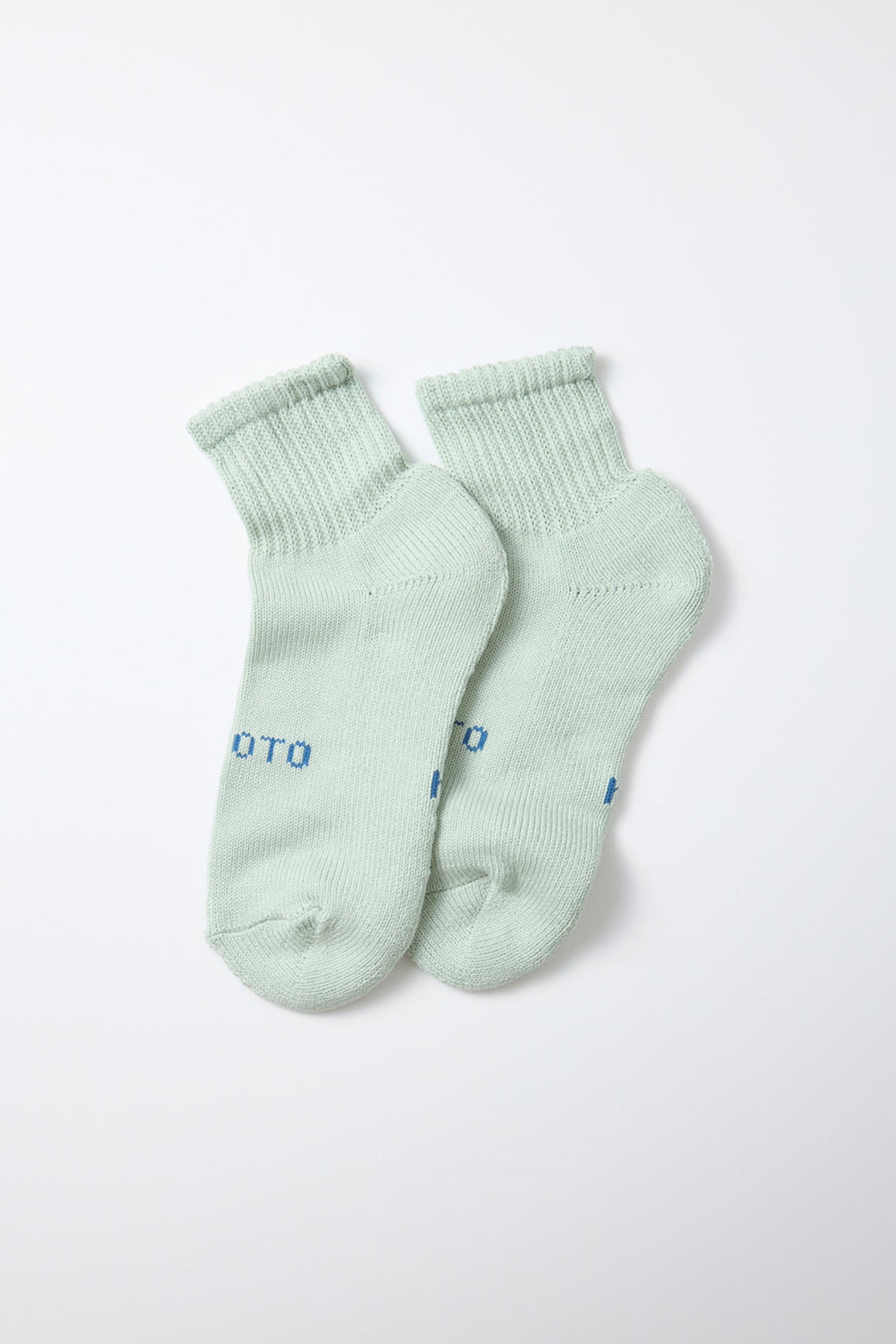 A pair of RoToTo Everyday Pile Ankle Socks in "Aqua," featuring ribbed cuffs, is displayed flat on a white background. Made in Japan, these light green socks have partially visible blue text near the toes from the RoToTo brand.