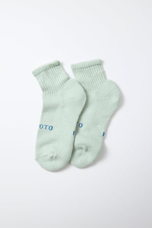 A pair of RoToTo Everyday Pile Ankle Socks in "Aqua," featuring ribbed cuffs, is displayed flat on a white background. Made in Japan, these light green socks have partially visible blue text near the toes from the RoToTo brand.