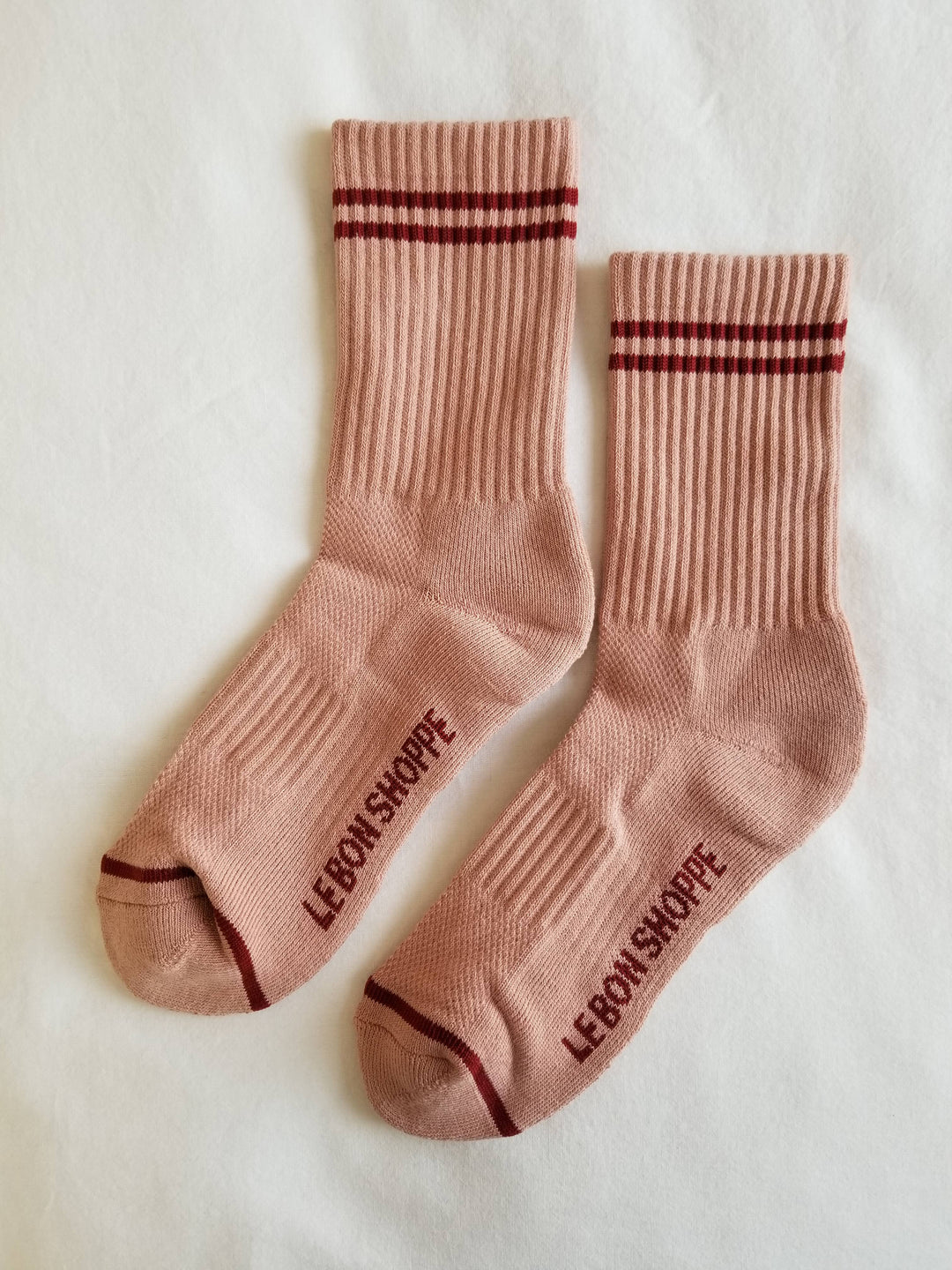 Le Bon Shoppe Boyfriend Socks in Vintage Pink, featuring light pink ribbed fabric, two red stripes at the top, red toe trim, and “LE BON SHOPPE” in red on the soles, shown on a white background.