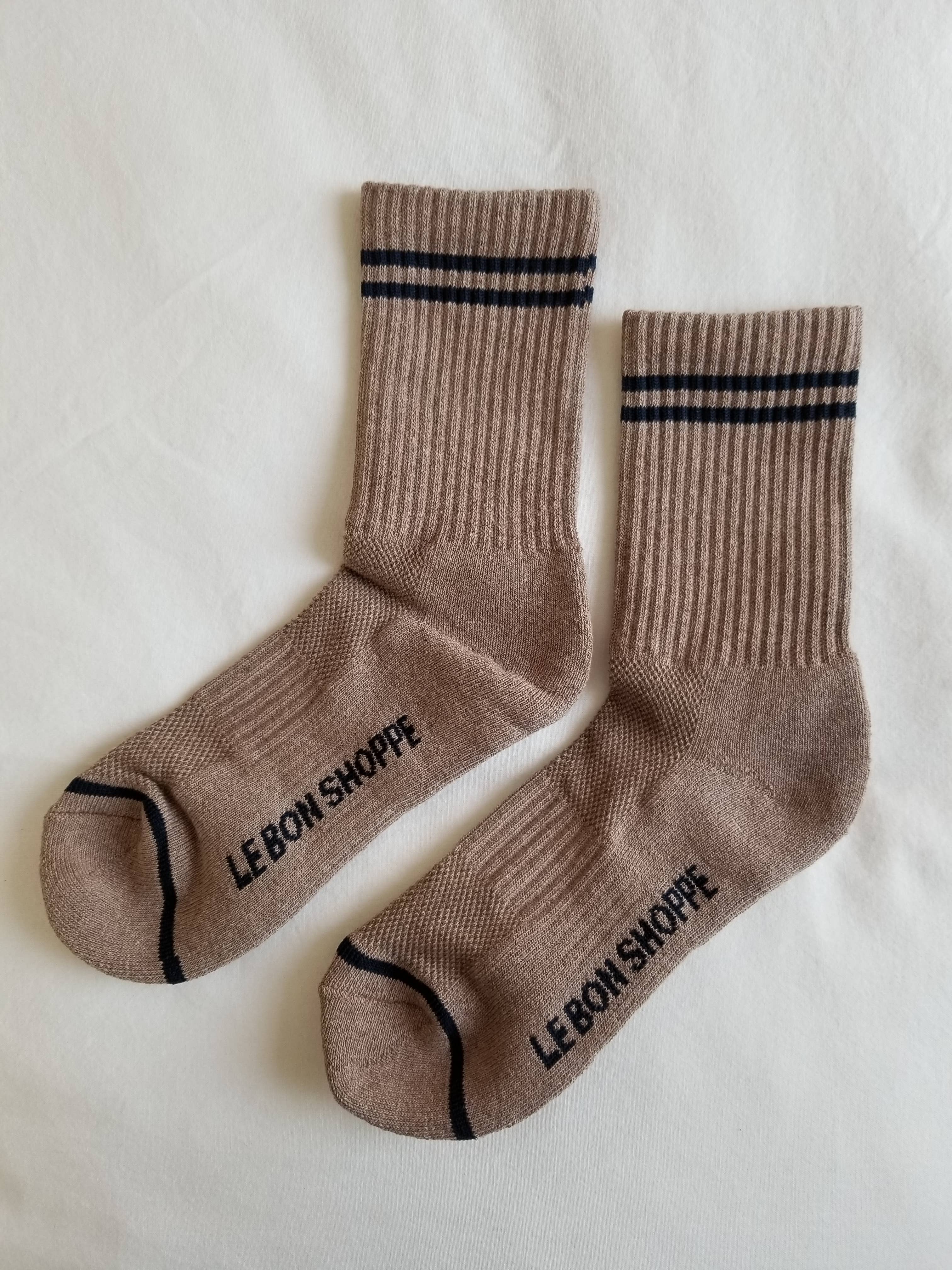 The Le Bon Shoppe Boyfriend Socks in Cocoa feature two black stripes near the top and "LE BON SHOPPE" printed on the soles, shown here on a white surface.