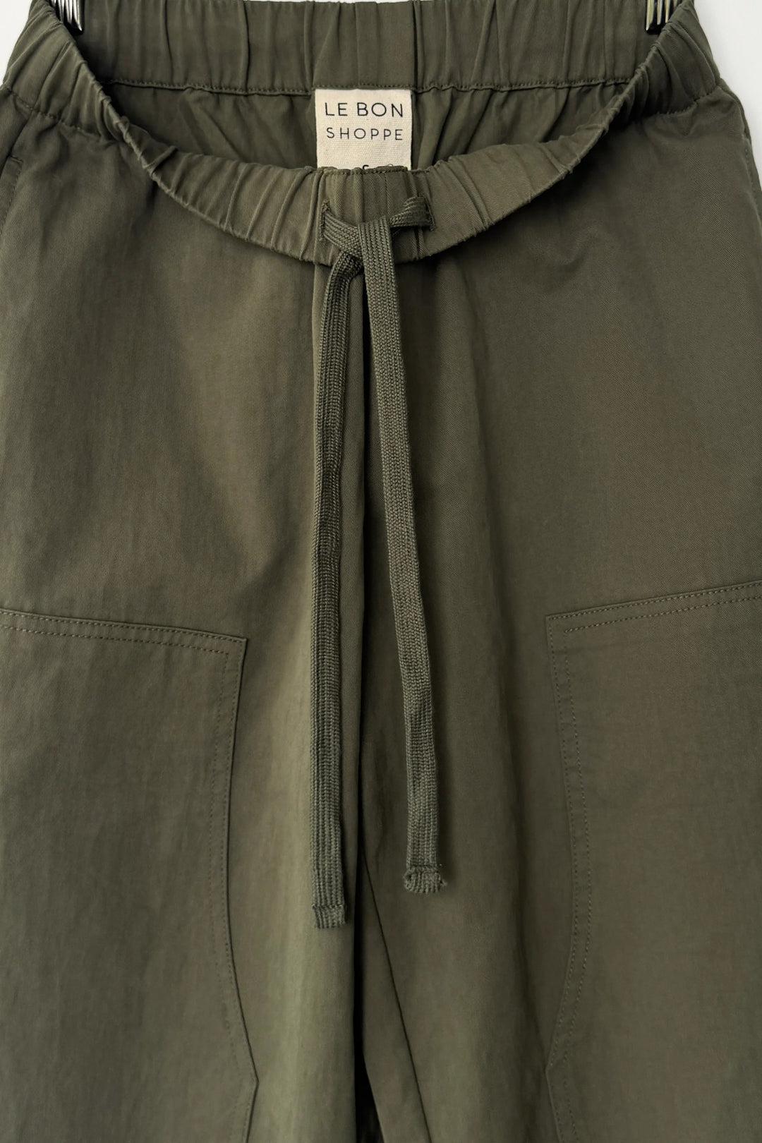The Le Bon Shoppe - Gardener’s Pant in Army Green features a relaxed silhouette with visible front pockets and a signature Le Bon Shoppe label on the waistband, crafted from lightweight cotton-nylon and shown hanging against a white background.