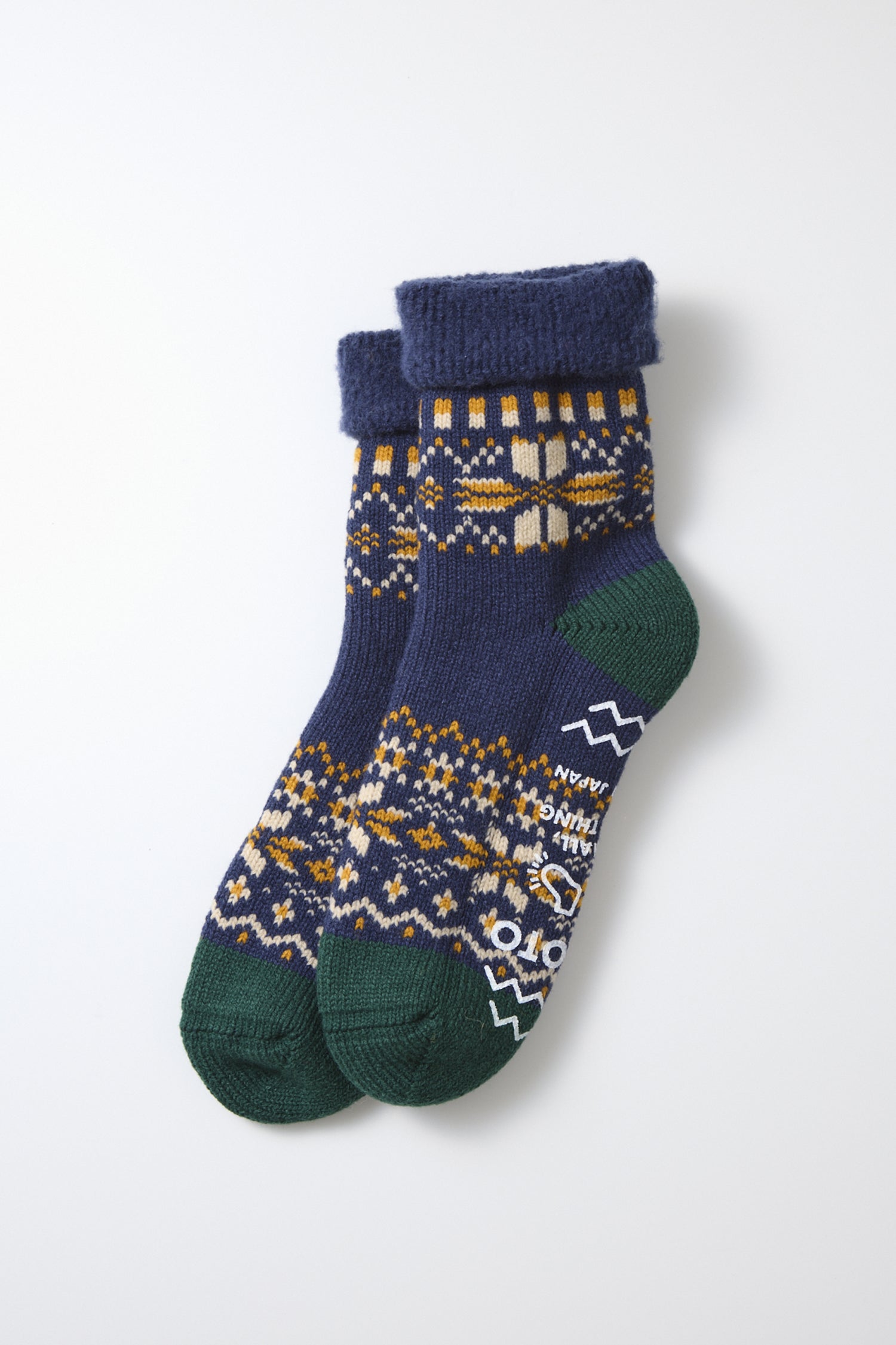 A pair of RoToTo Comfy Room Snow Flake Socks in navy, featuring green toes and heels, a yellow and white geometric pattern, and folded cuffs, made in Japan by RoToTo, displayed on a white background.