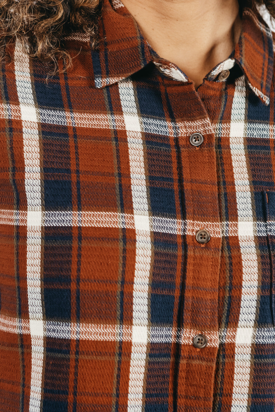 Close-up of a person wearing the Bridge & Burn Ash Slim Shirt in Echo Ridge Plaid; part of their curly hair and neck are visible.