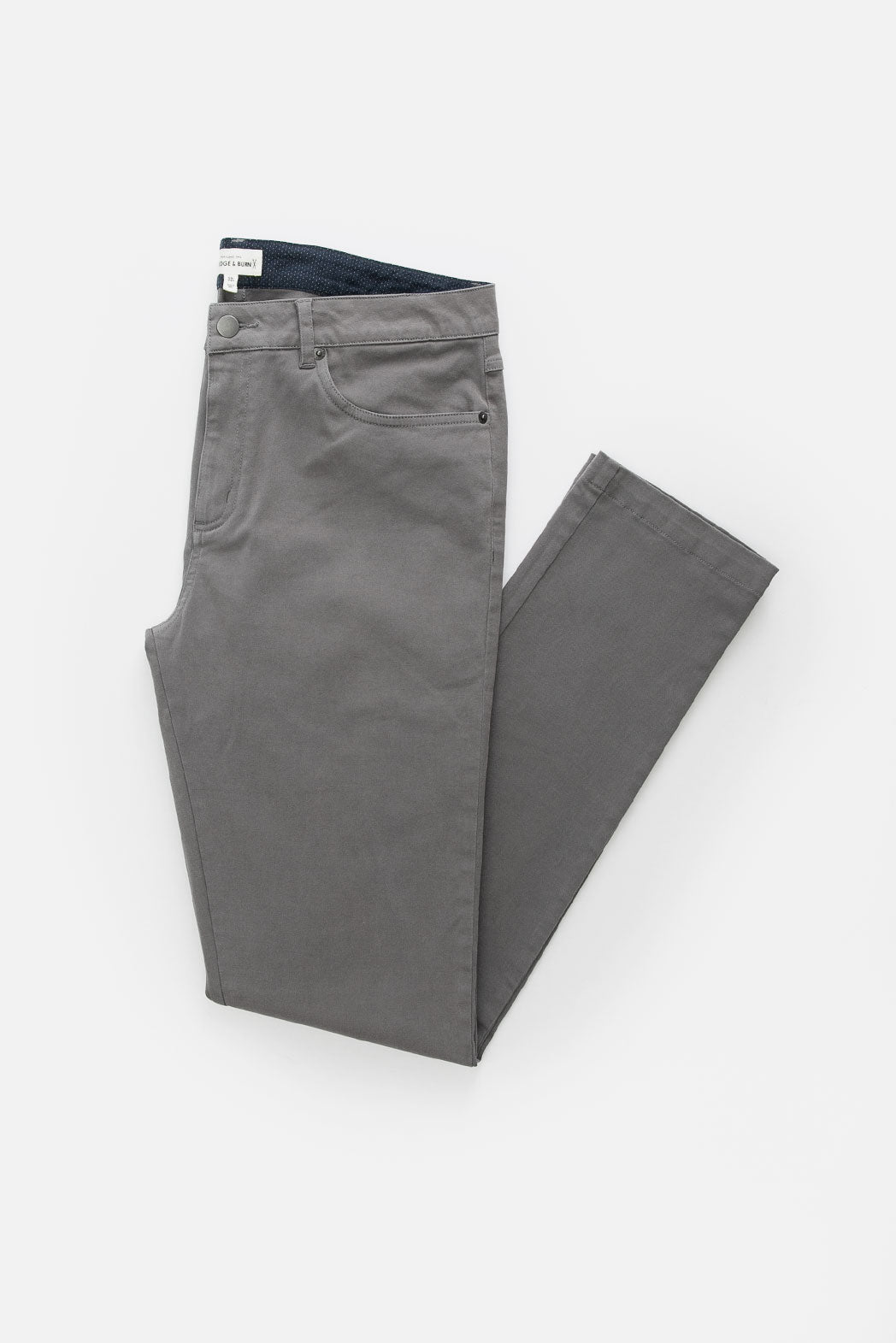 The Bridge & Burn Bradley Slim Pant in grey, neatly folded on a white background, highlights its classic 5-pocket design with visible front pocket, waistband, and a glimpse of the inner lining.