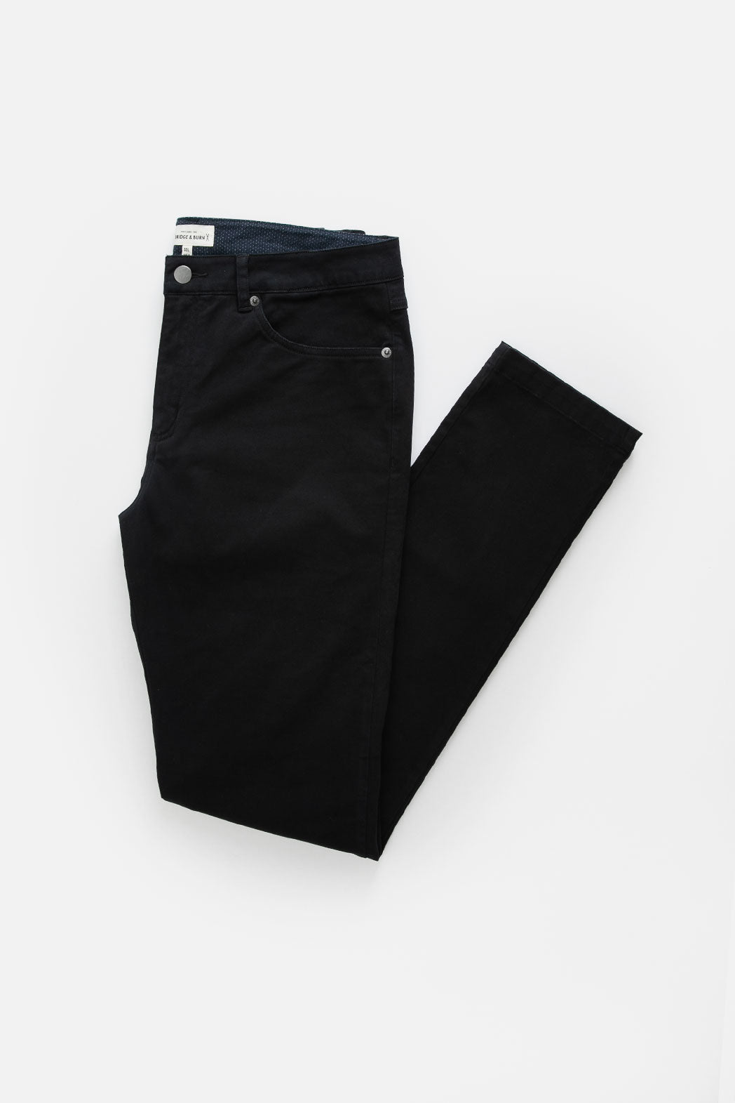 The Bradley Slim Pant in black by Bridge & Burn features a classic 5-pocket design, button closure, and front pockets. Made from organic cotton, these men's slim fit pants are shown neatly folded on a plain white background.
