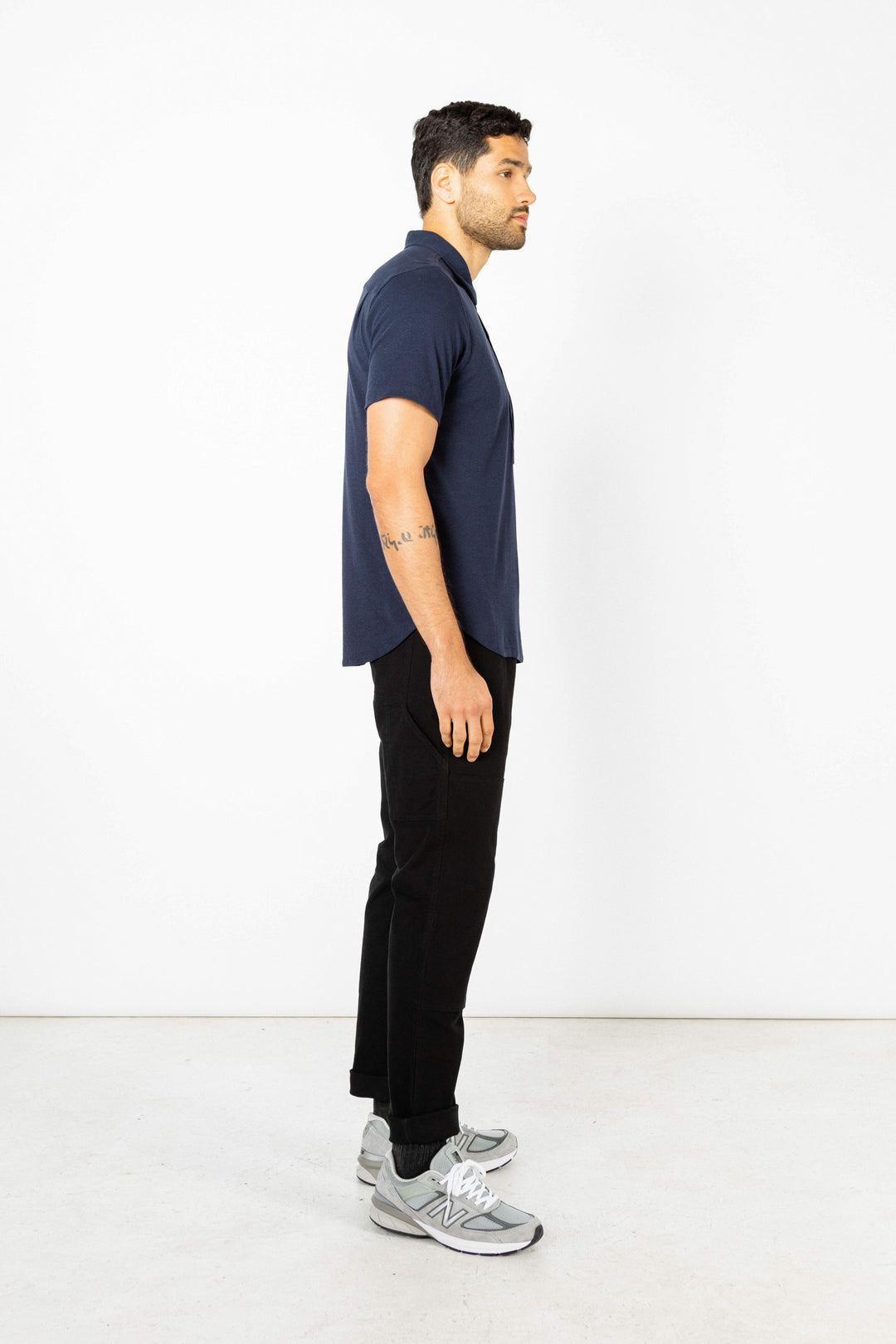 A man in profile faces left against a plain white background, wearing the Bridge & Burn Gary Knit Pullover in navy jersey, black pants, and gray sneakers.